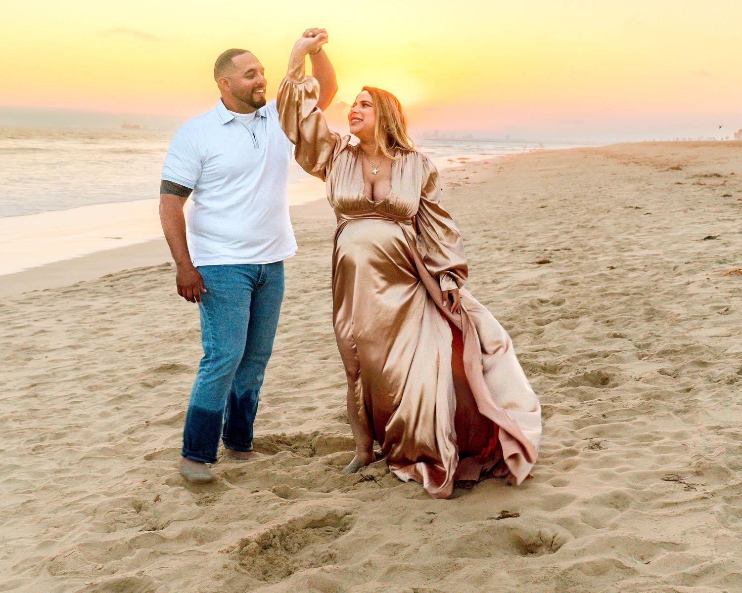 Couple dancing together on a beach at sunset wearing formal attire.