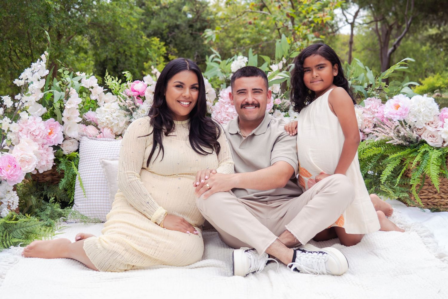 A couple lounges on a white blanket surrounded by pink floral decorations in an outdoor setting.