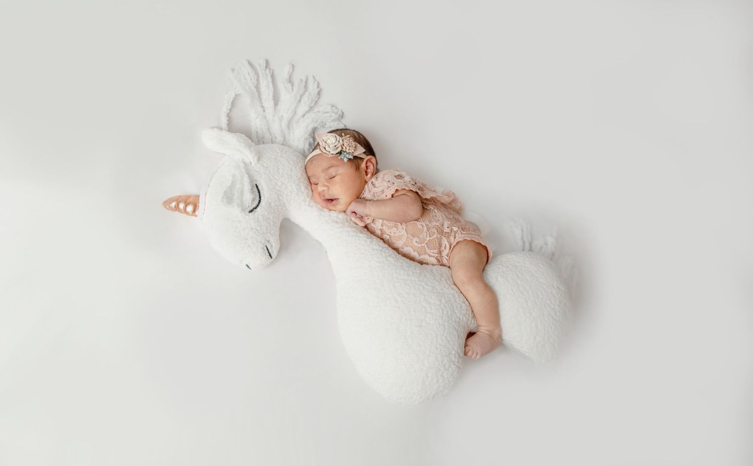 Newborn baby lying in white linen with small decorative dove figurine on star patterned background.