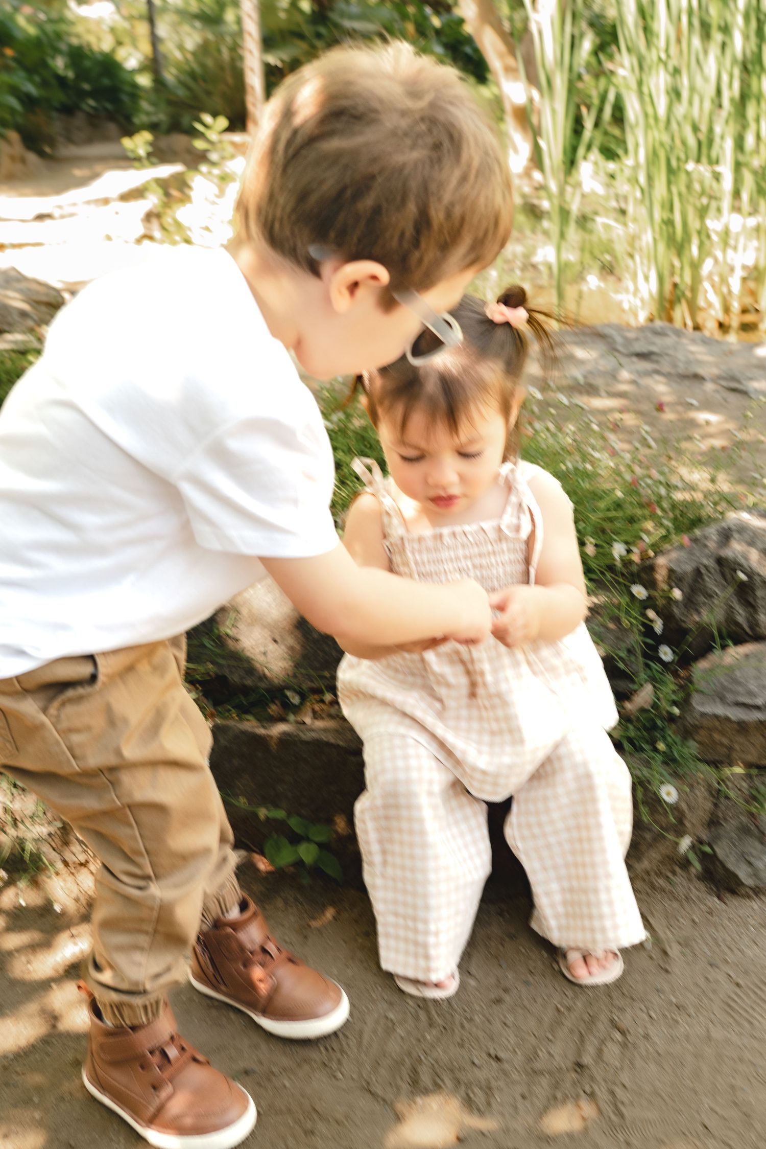 Small children in casual attire play together on a stone path surrounded by greenery.