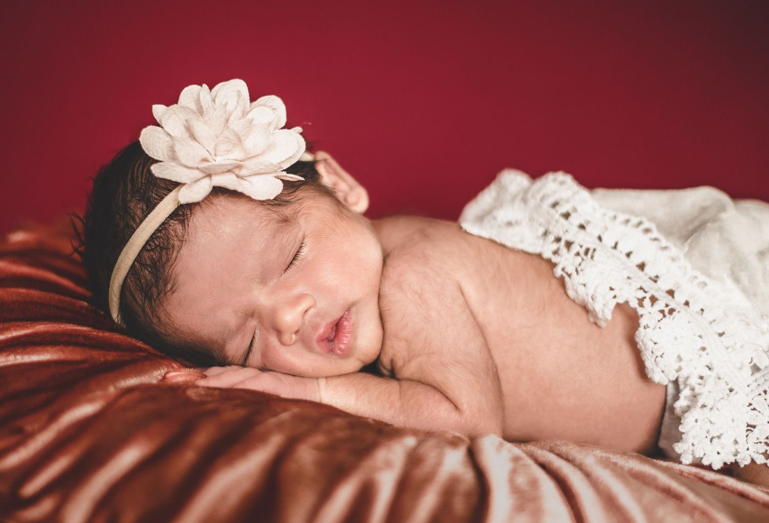 Baby sleeping on red silk fabric with delicate white flower decoration.