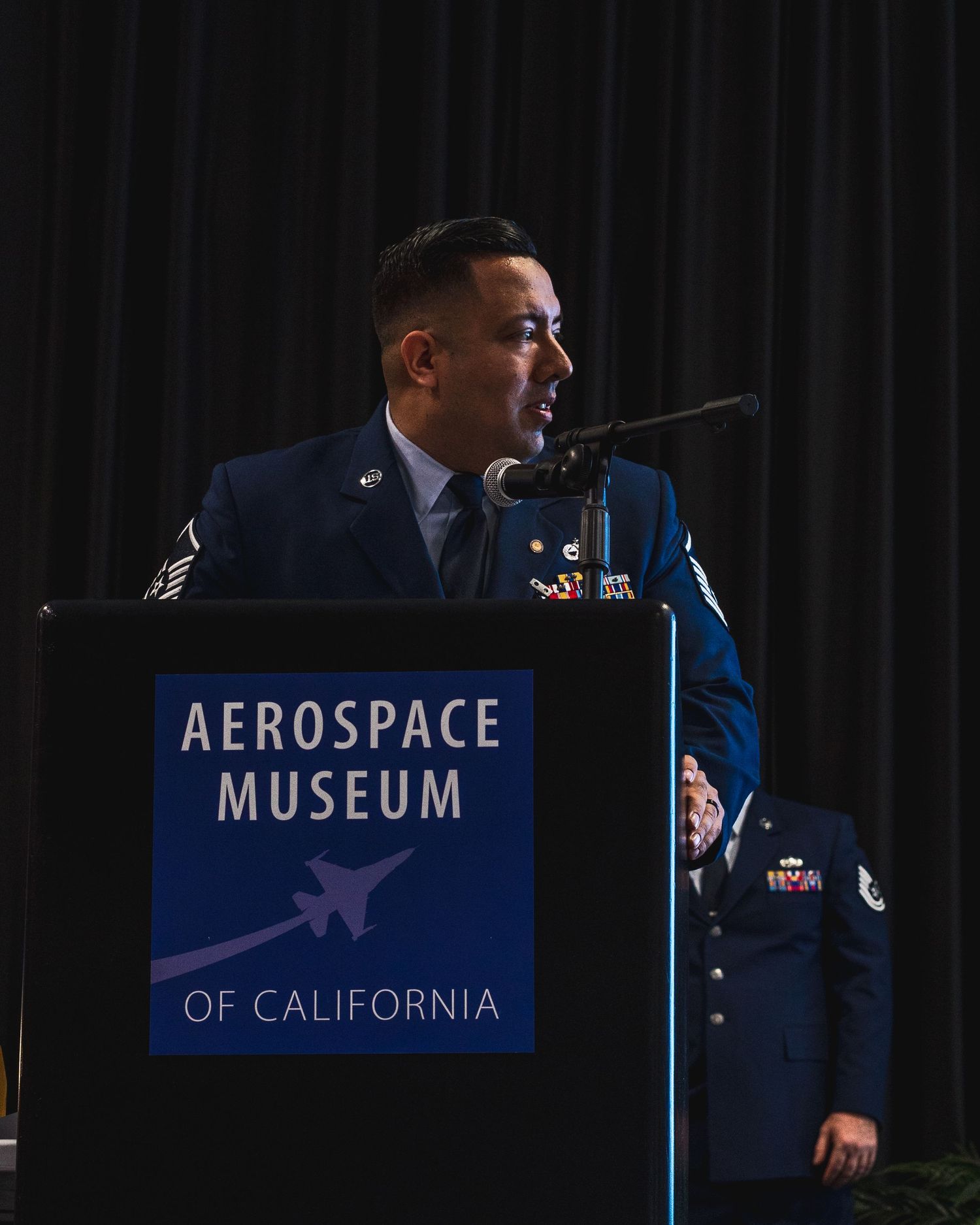 Air Force staff sergeant speaks at podium at Aerospace Museum of California ceremony.