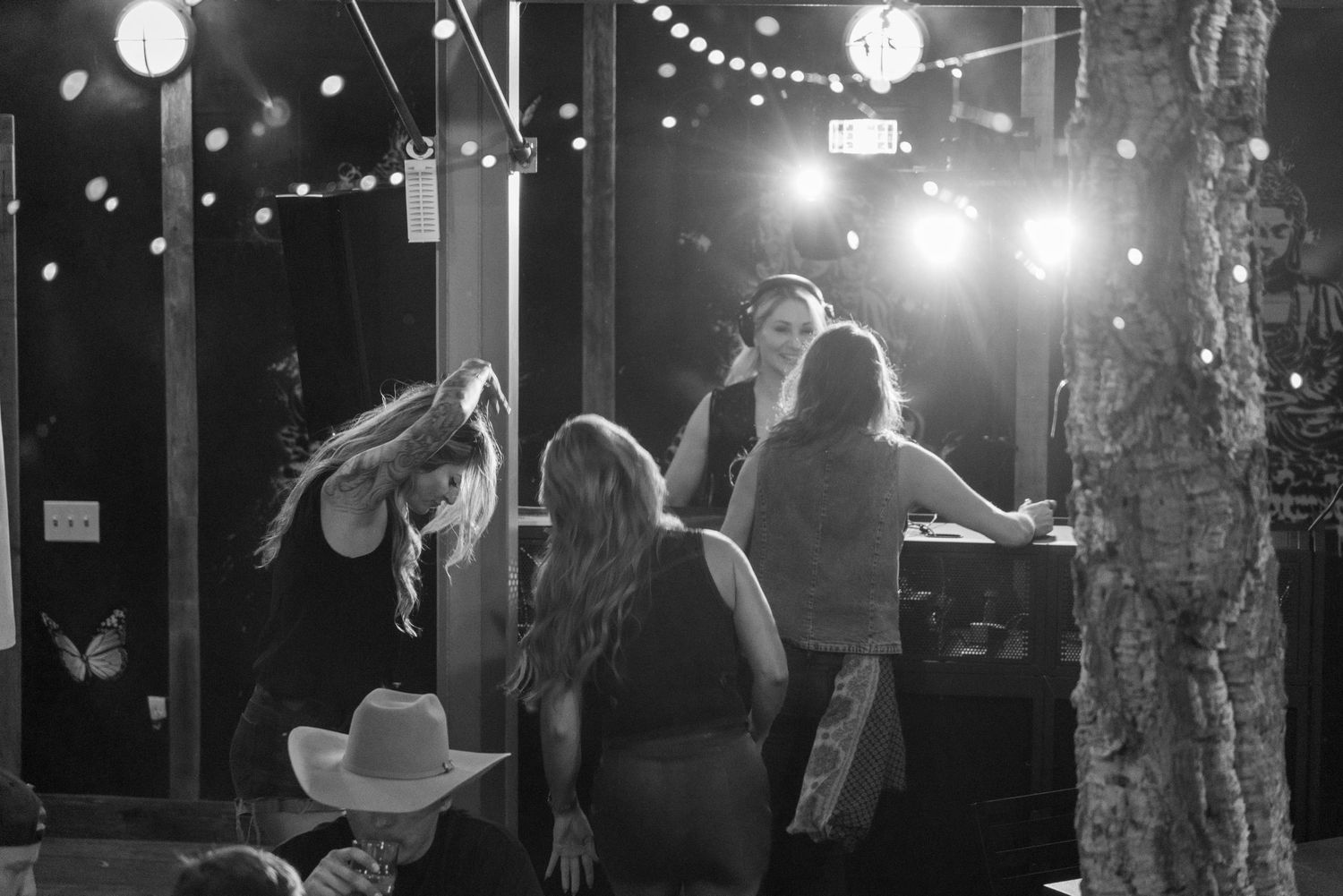 Black and white photo of women gathered near a bar under string lights at an outdoor night event.