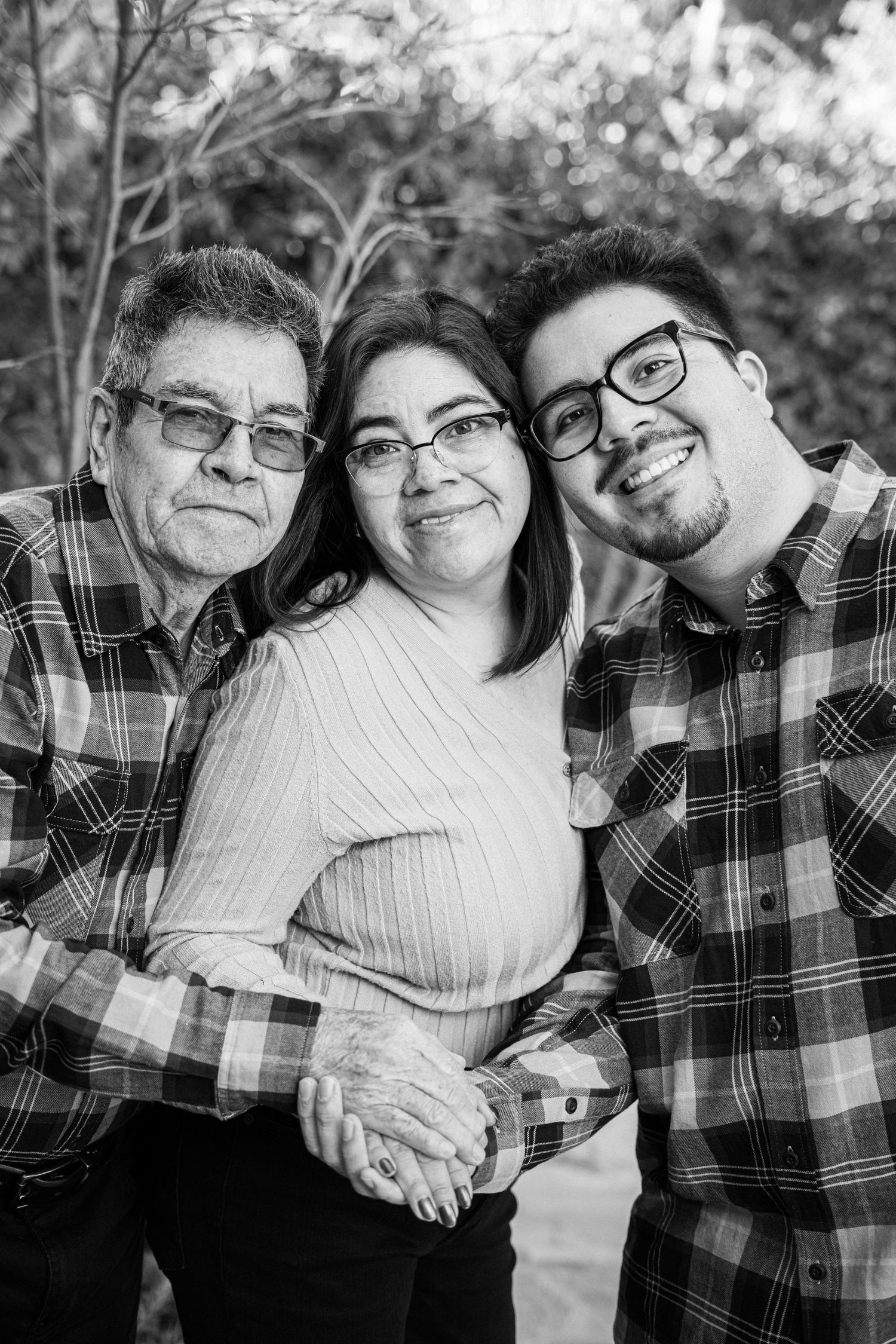 Black and white family portrait with matching plaid shirts against natural outdoor background.