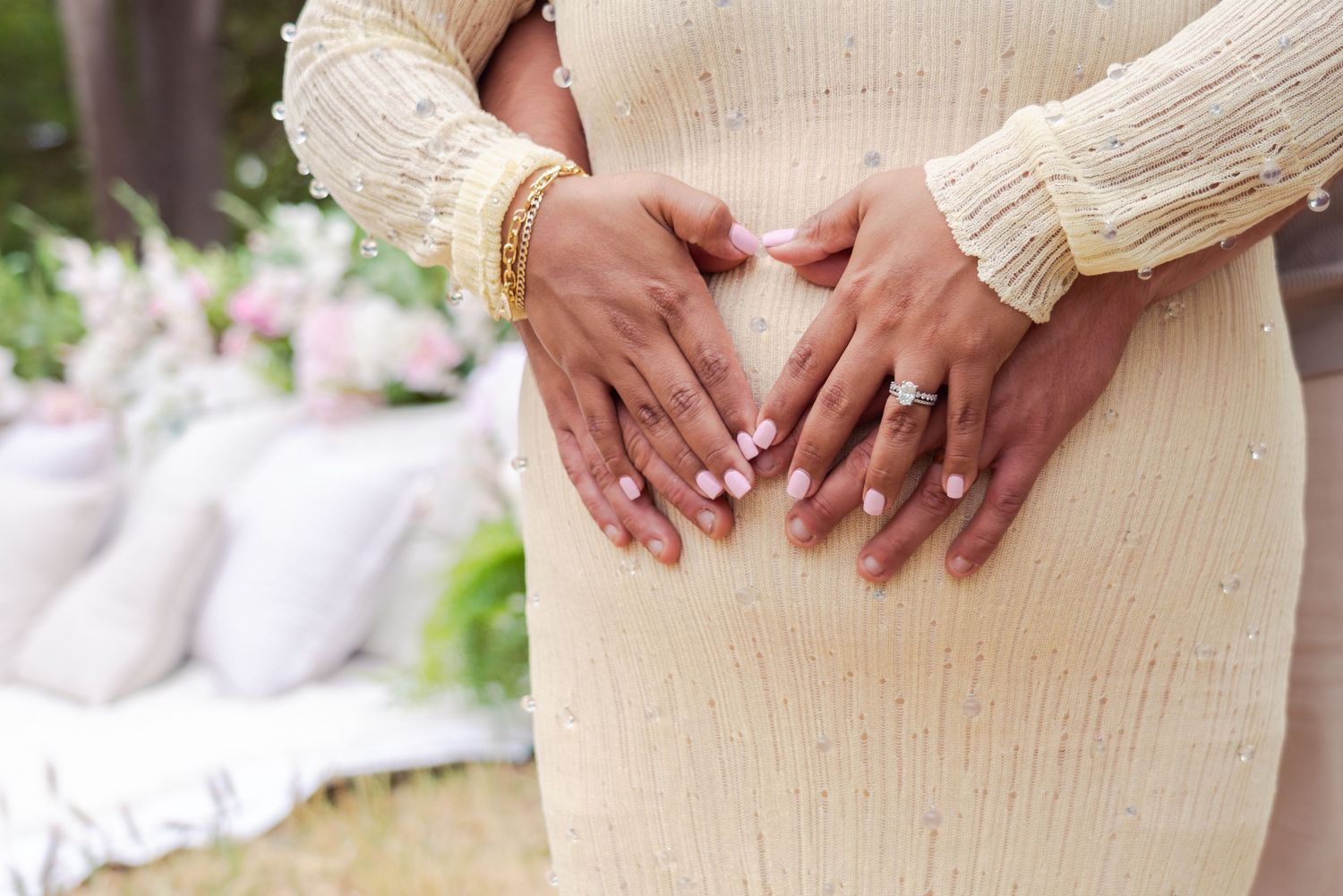 Close-up shots of hands cradling pregnant belly in cream knit dress.