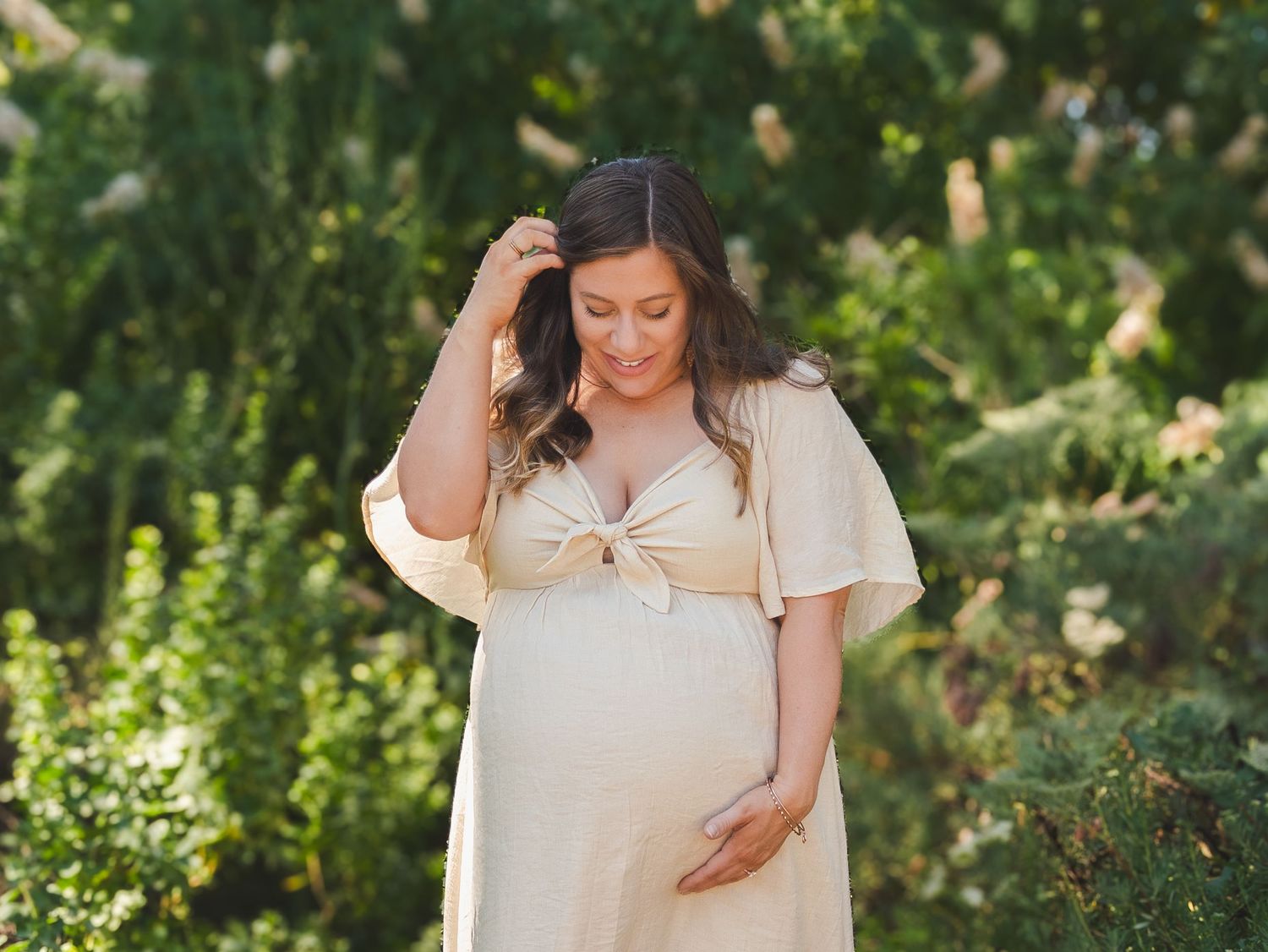 Maternity garden photoshoot with woman in cream dress among blooming flowers.