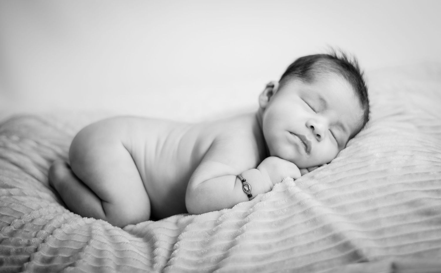 Black and white portrait series of sleeping newborn on textured bedding.