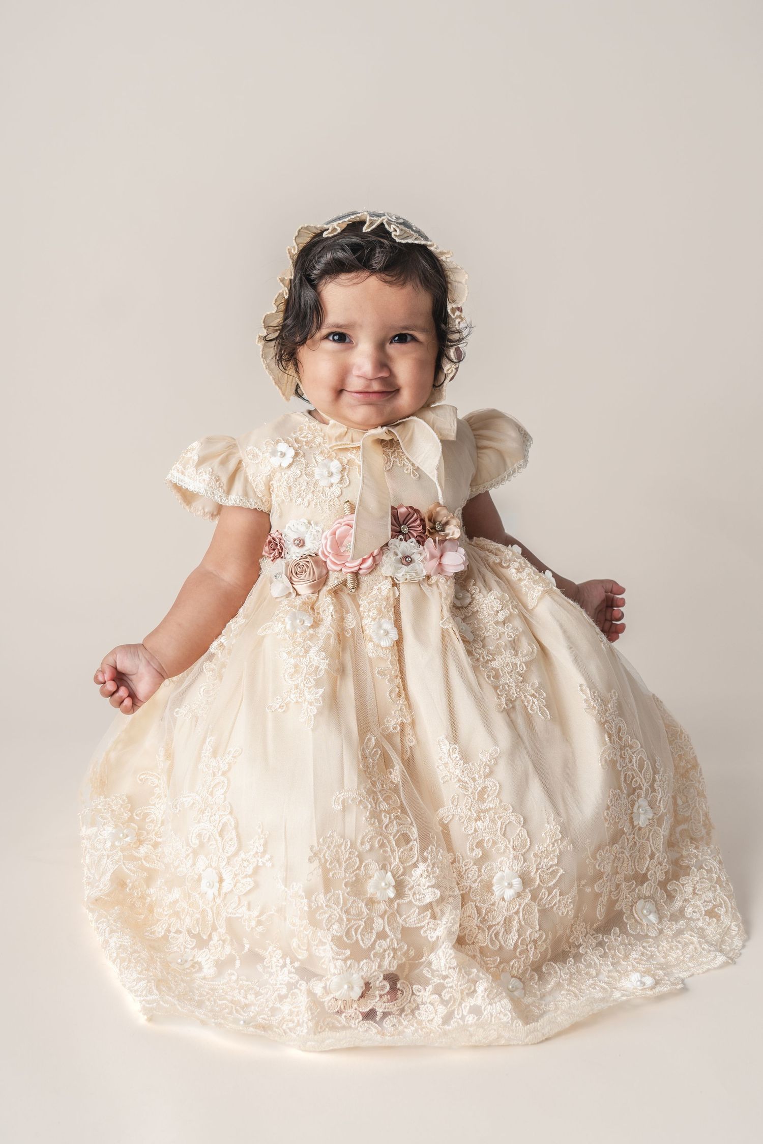 A child in an ornate ivory christening gown with lace details and floral embellishments.