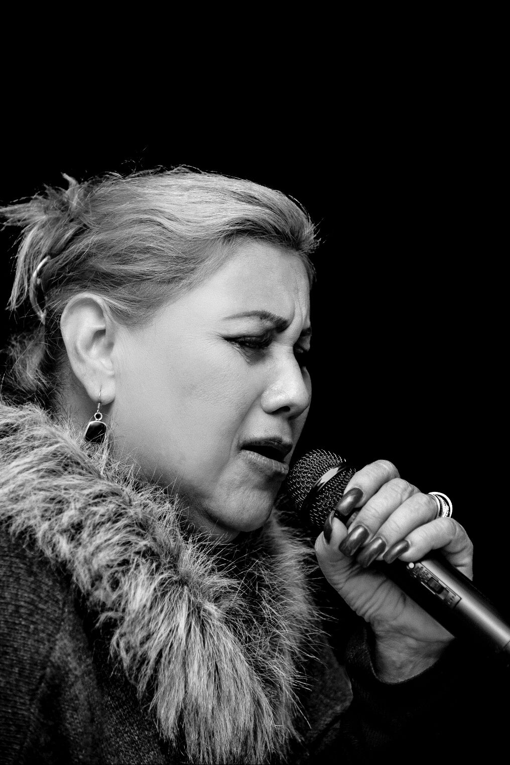 Black and white photo series of a performer singing emotively into a microphone wearing a fur collar.