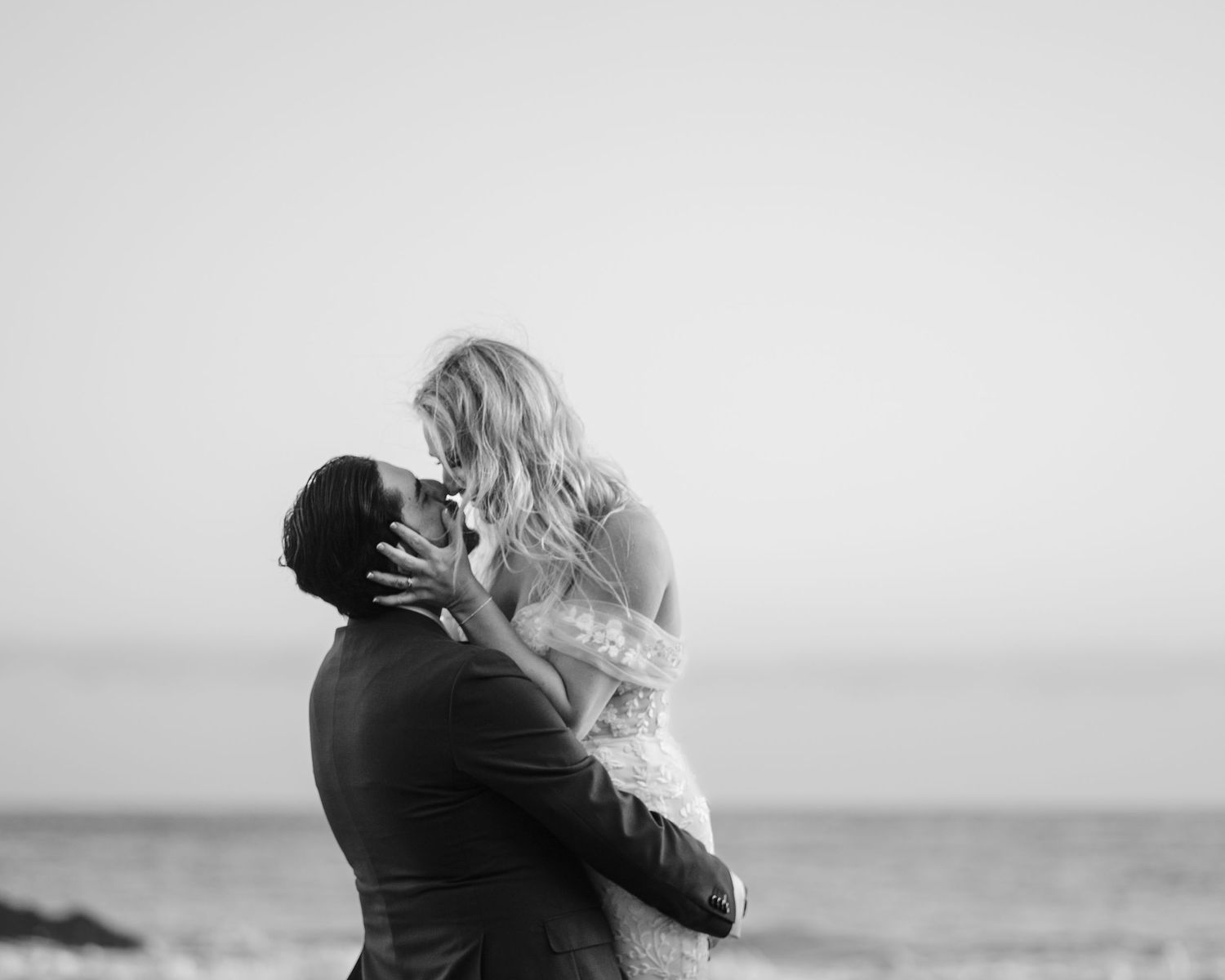 A romantic black and white photo series showing a couple embracing and kissing at the beach.