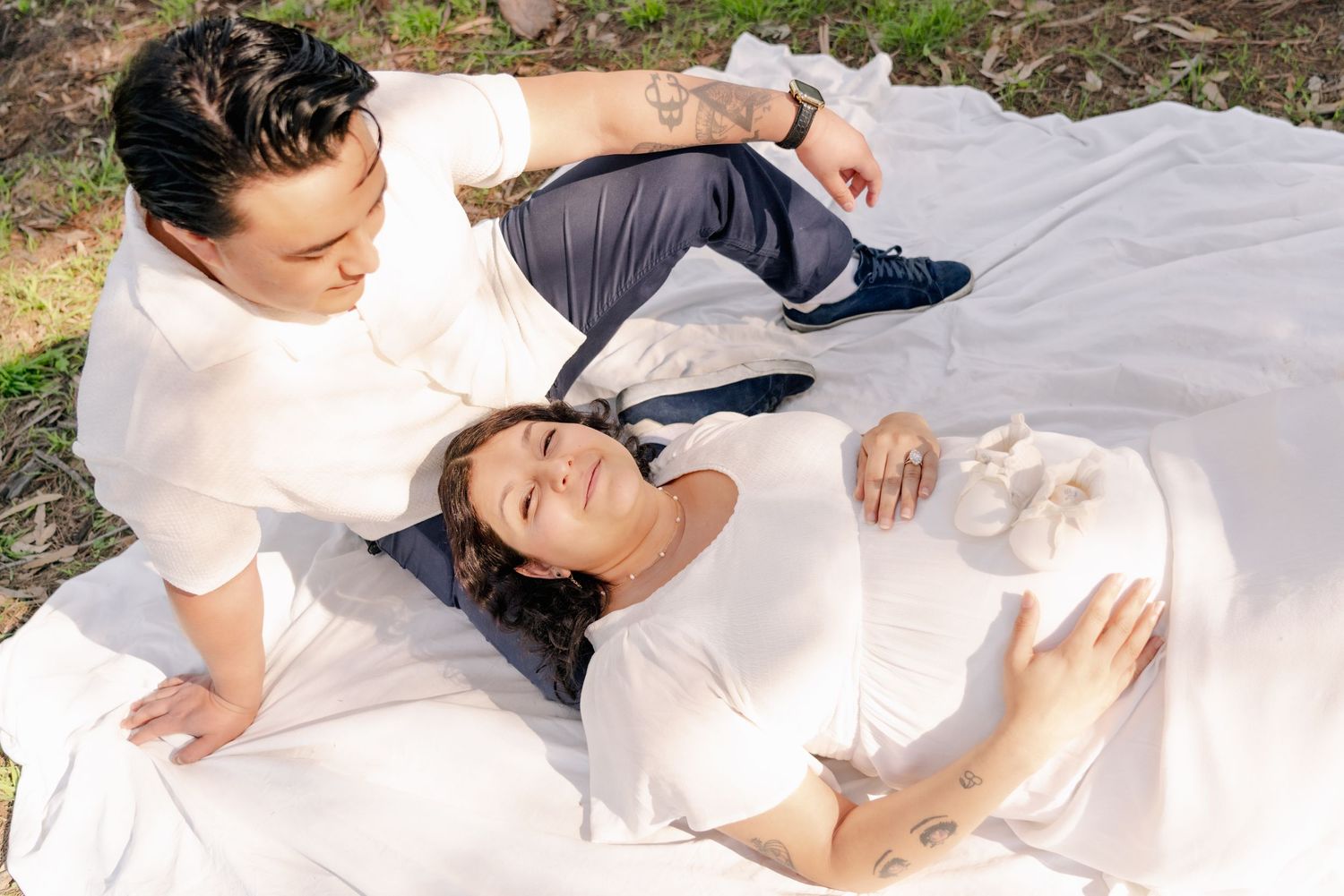 A family relaxes together on a white blanket during an outdoor photo session.