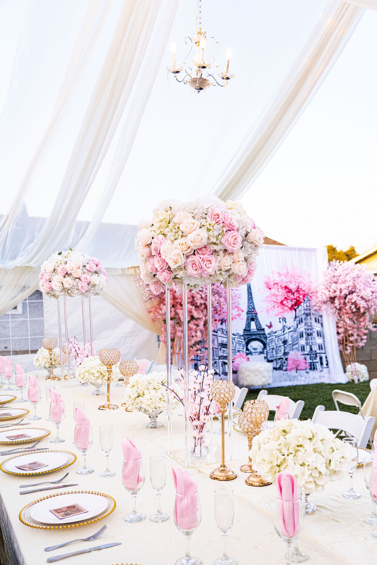 Elegant table setup with pink flowers, gold accents, and Eiffel Tower motifs under white tent draping.
