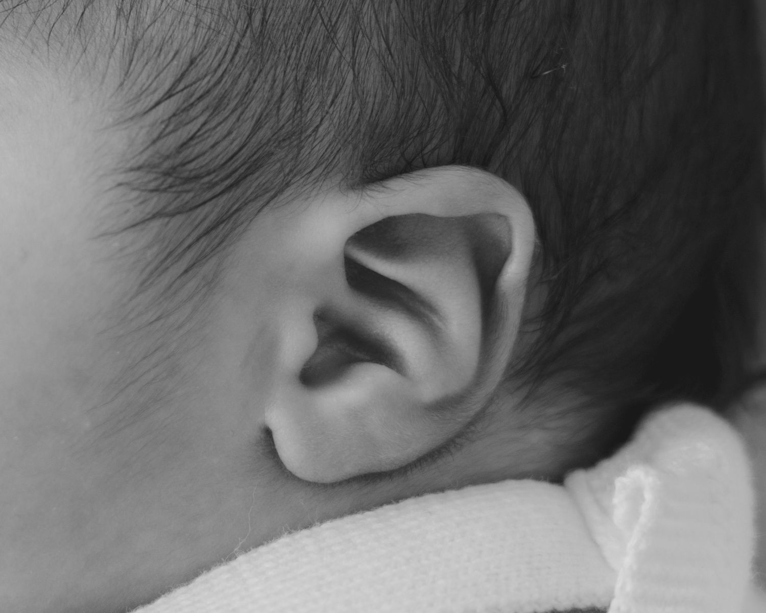 Close-up black and white photo of a newborn baby's ear and dark hair.