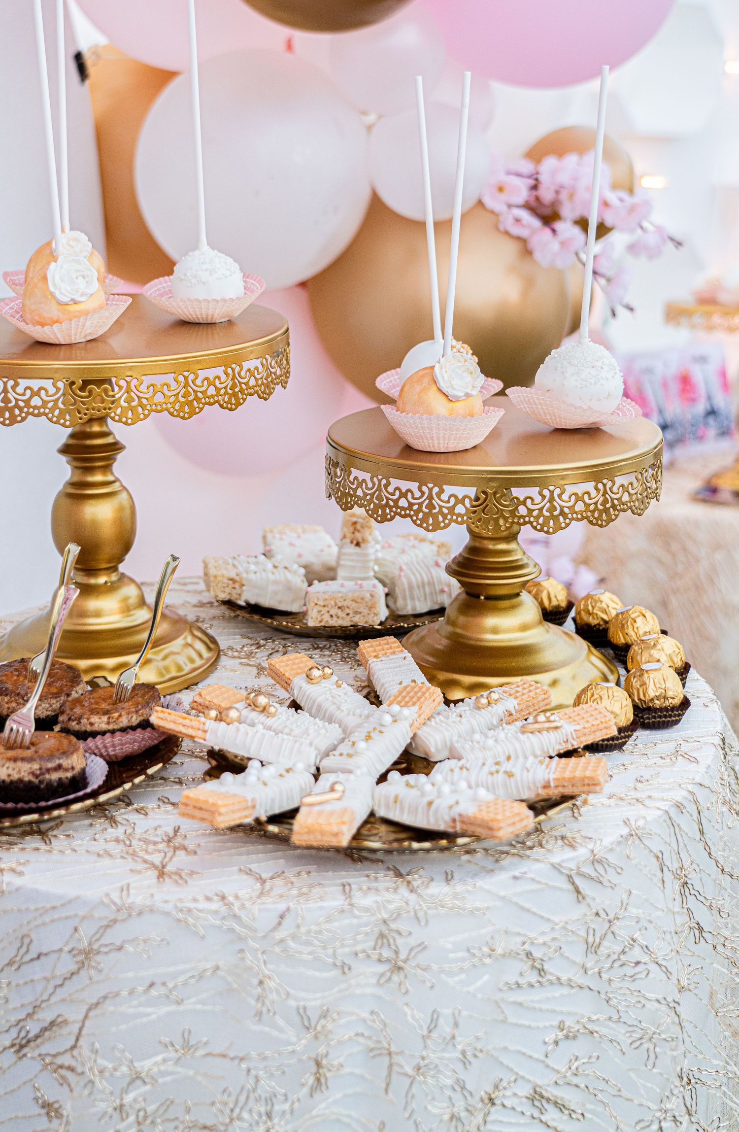 Ornate gold cake stands displaying delicate desserts and treats on a textured tablecloth.