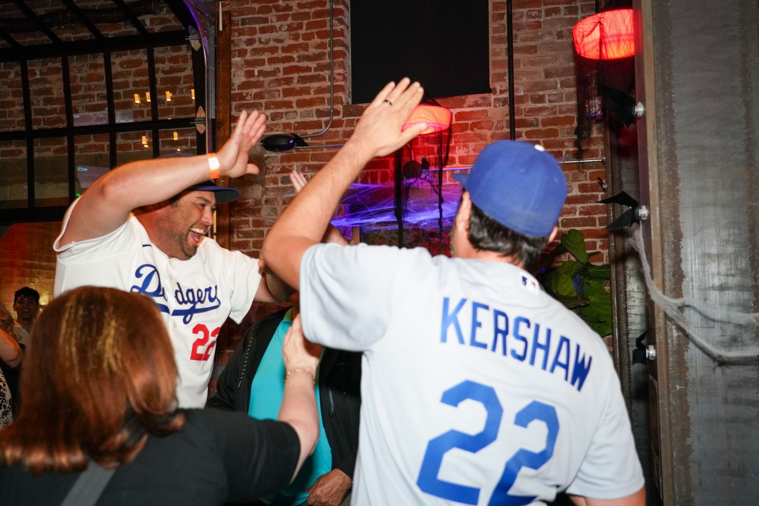 Two Dodgers fans in Kershaw #22 jerseys high-fiving at a lively sports bar celebration.