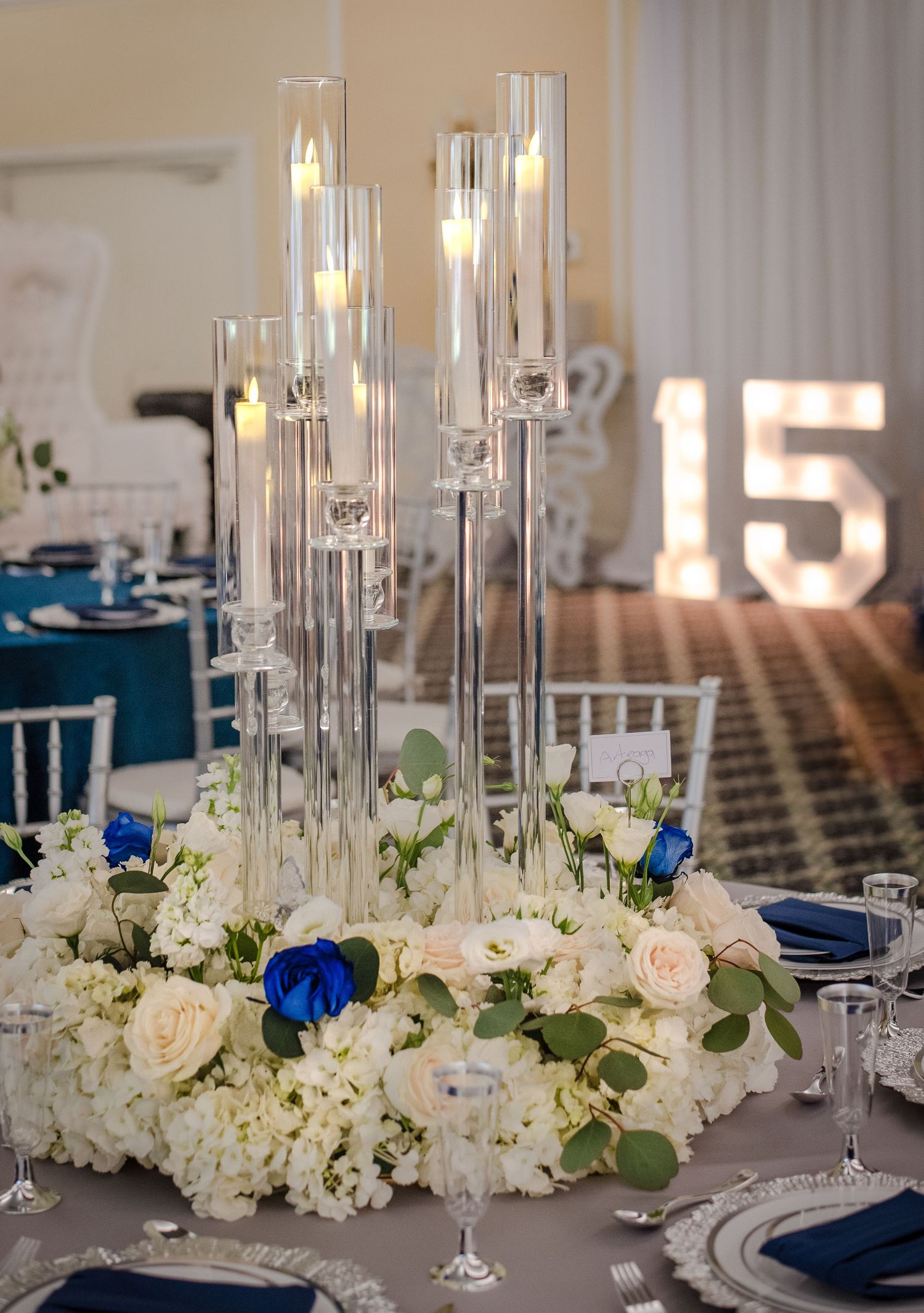 White floral centerpieces with tall glass candleholders decorate elegant navy blue tablescapes.