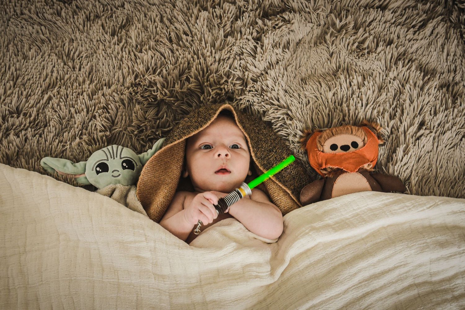 Baby resting on textured grey bedding with plush toys.