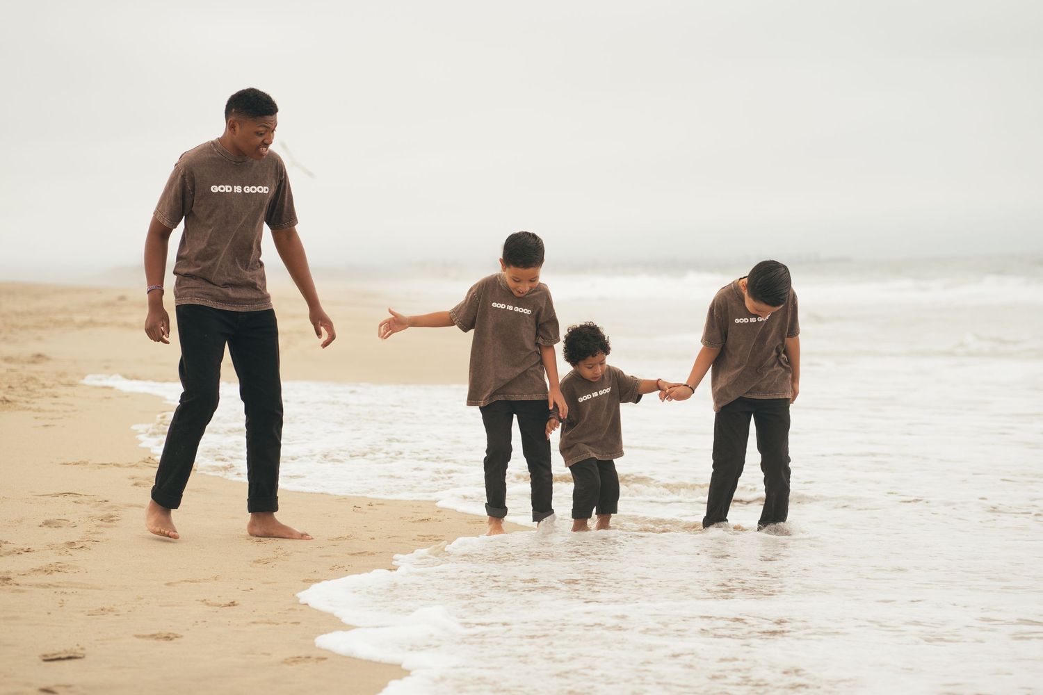 Family of four in matching brown shirts walking along a sandy beach shoreline together.