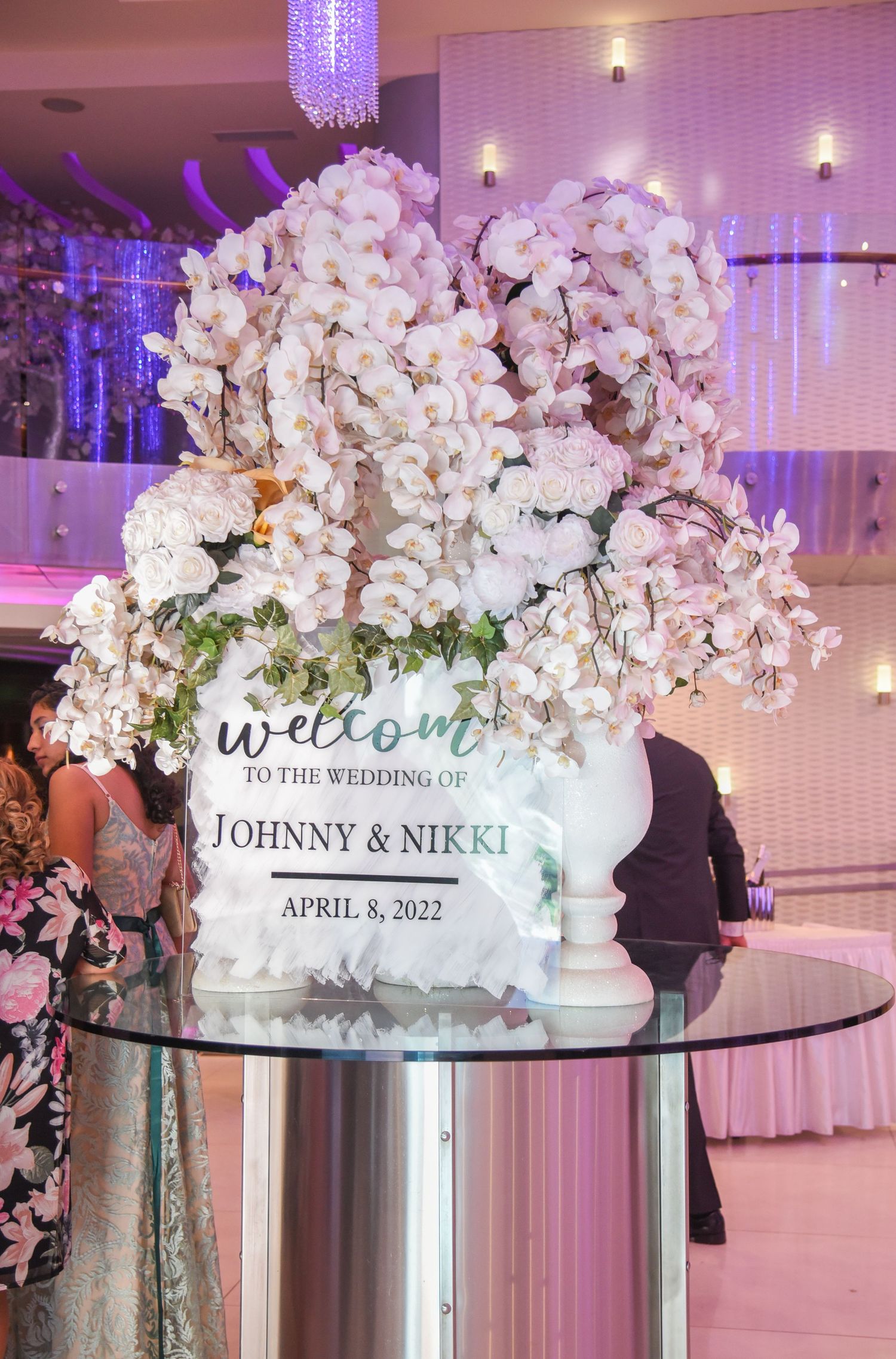Luxurious white floral welcome sign display with orchids and roses at a wedding entrance.