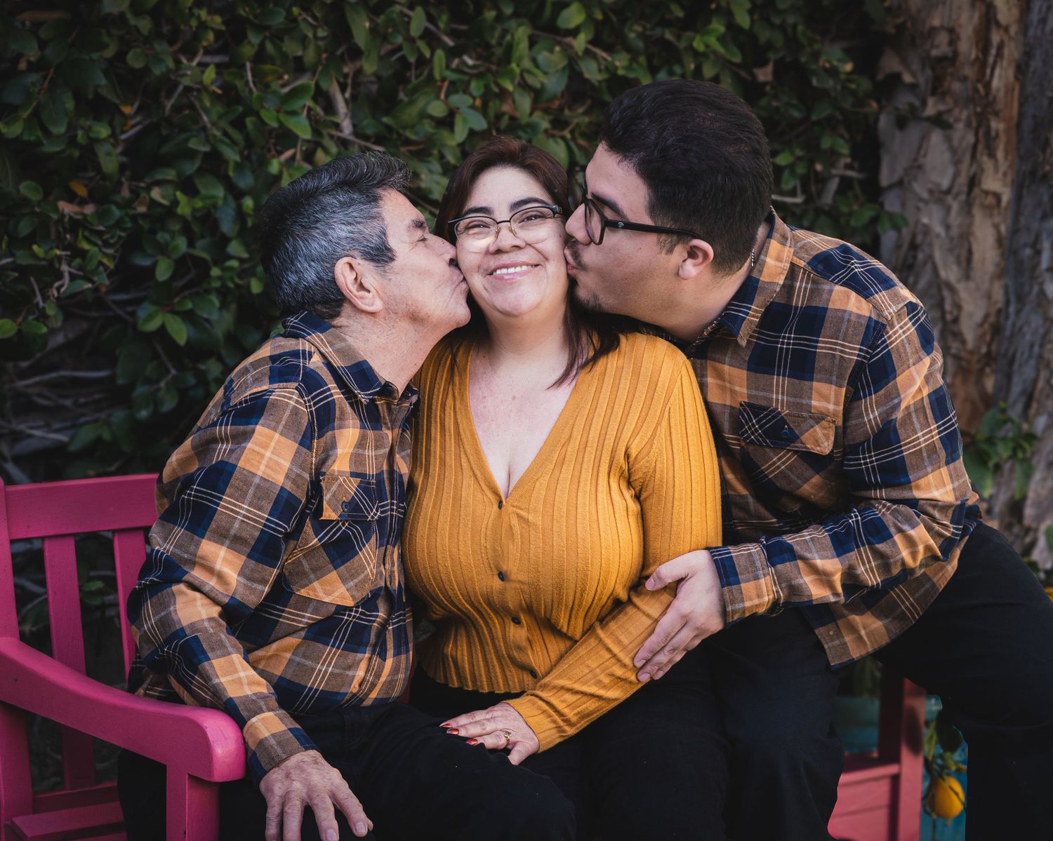 Joyful family moment on red bench with matching plaid shirts and yellow sweater in garden setting.