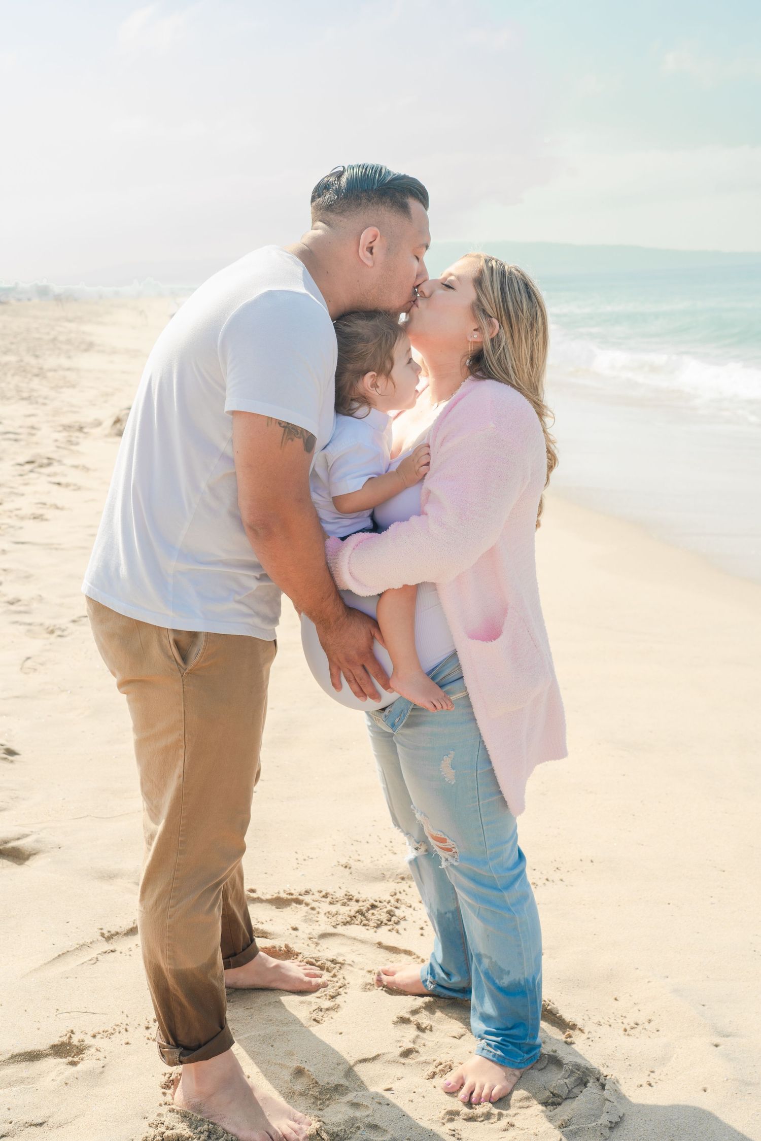 Tender family moments captured on a sunny beach with ocean waves in the background.