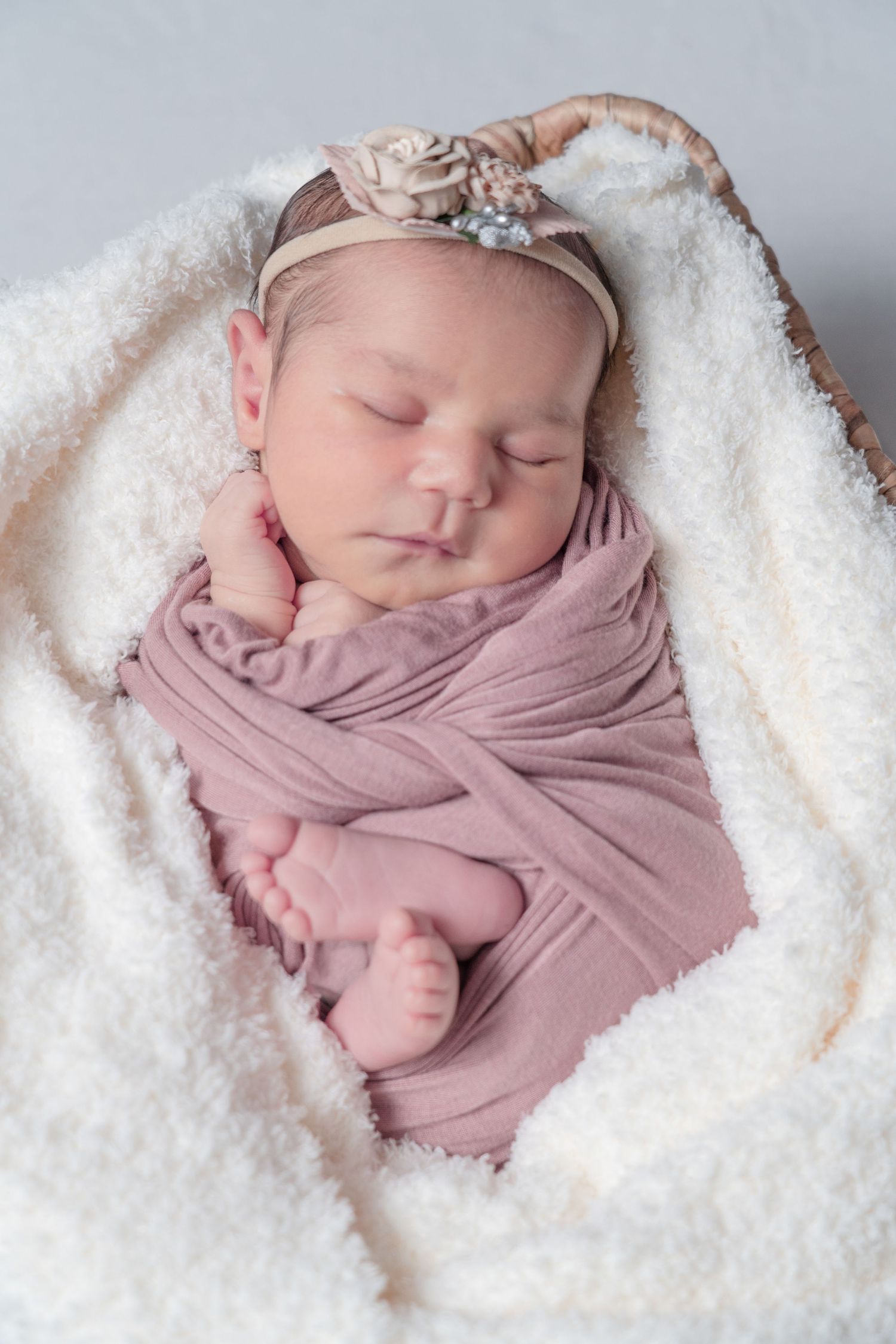 A sleeping newborn wrapped in soft pink swaddle against white fluffy blanket.