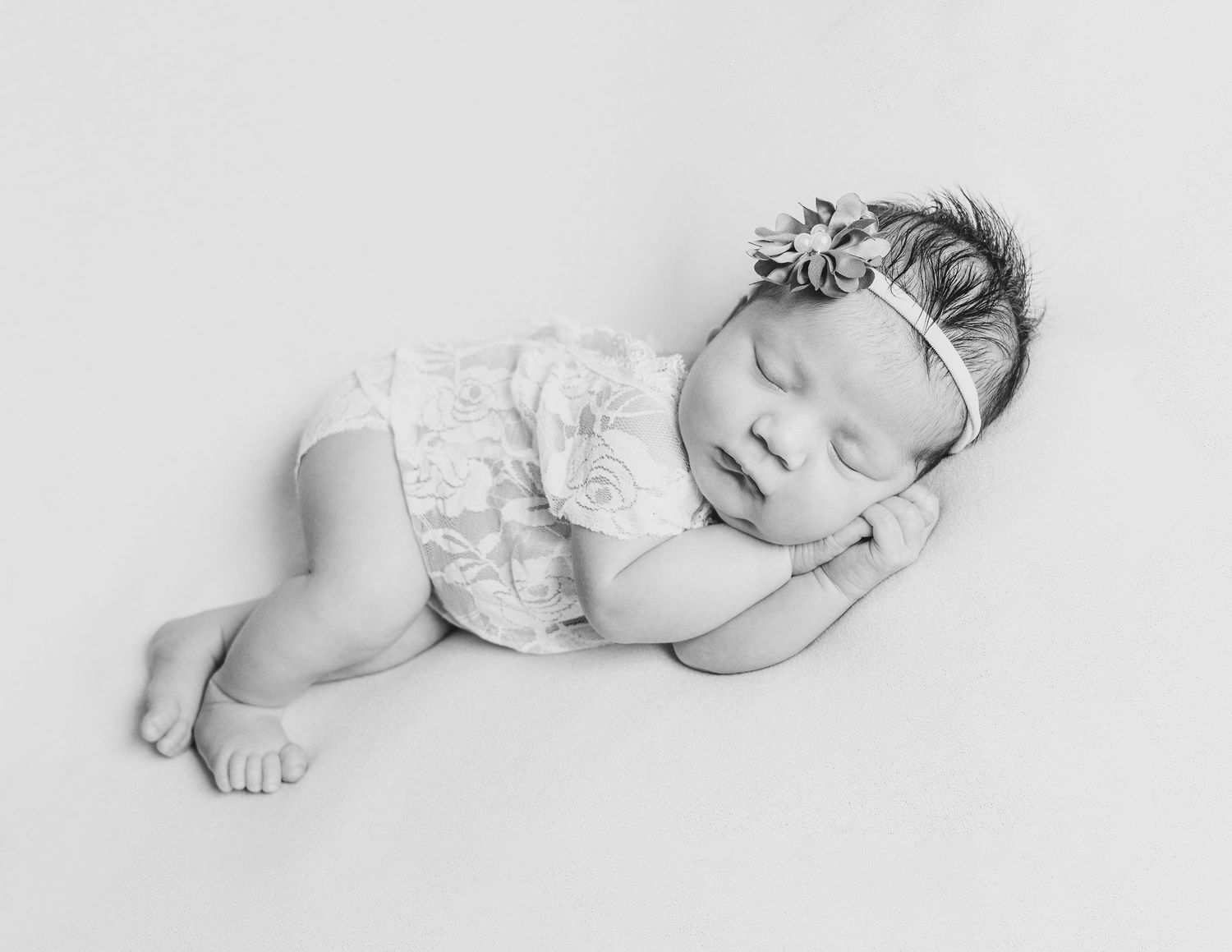 Black and white portrait of sleeping newborn in lace outfit with floral headband.