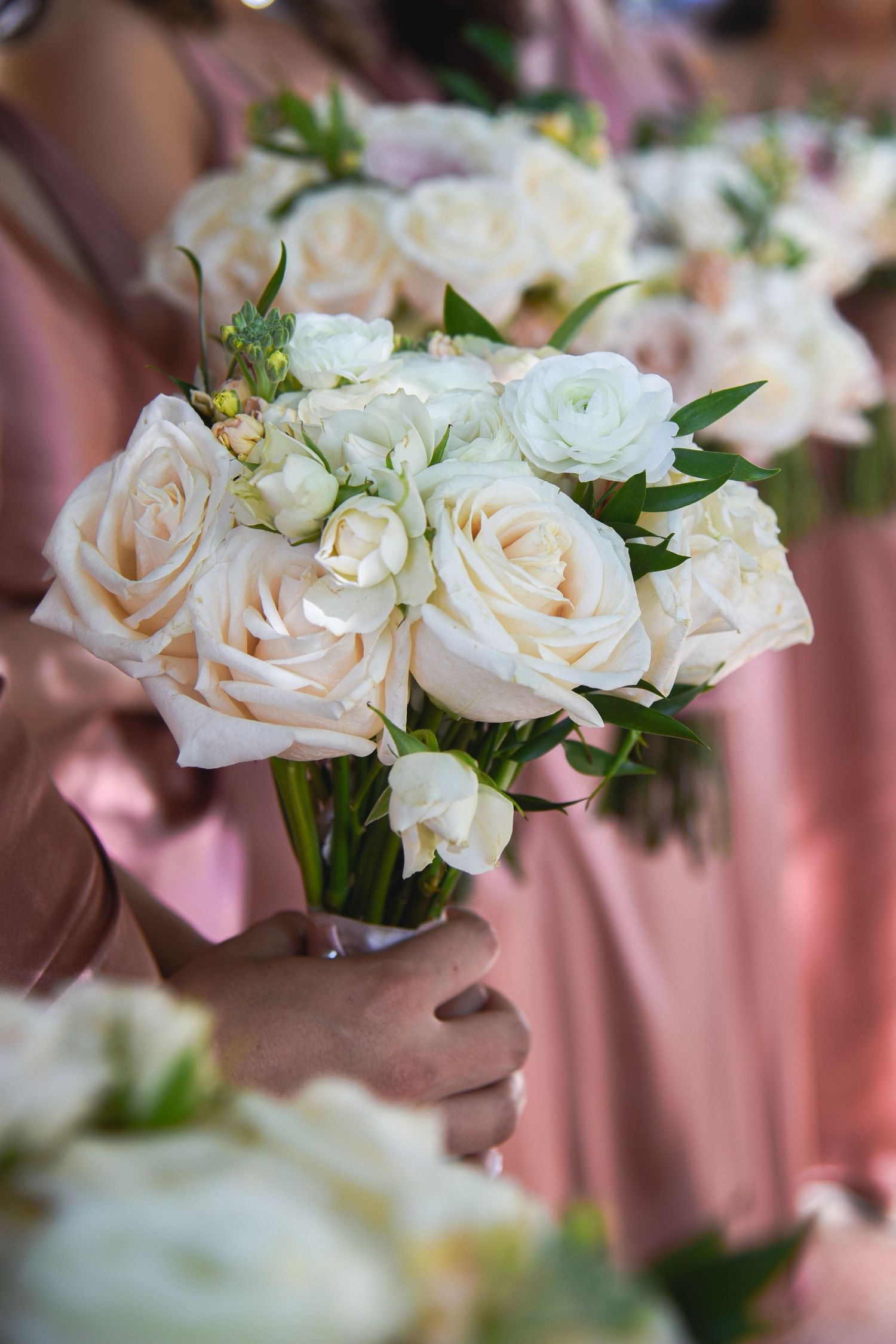 Elegant white and blush rose bouquets arranged in a line with soft pink background.