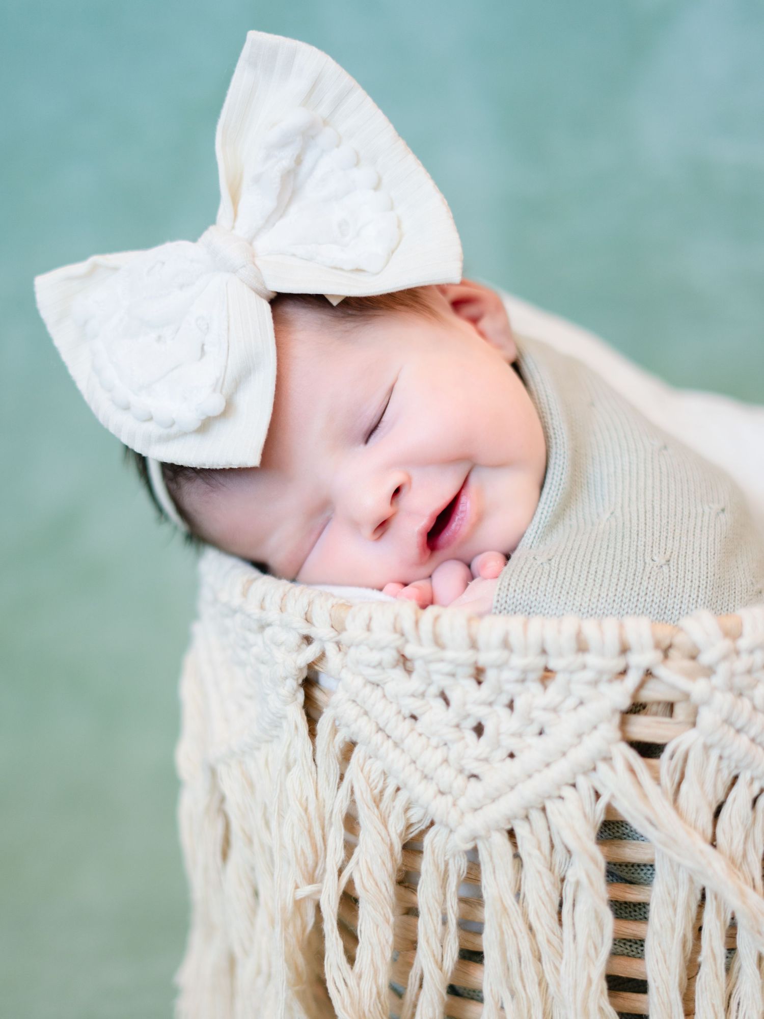 A newborn baby sleeping on a macrame hammock with a white bow headband.