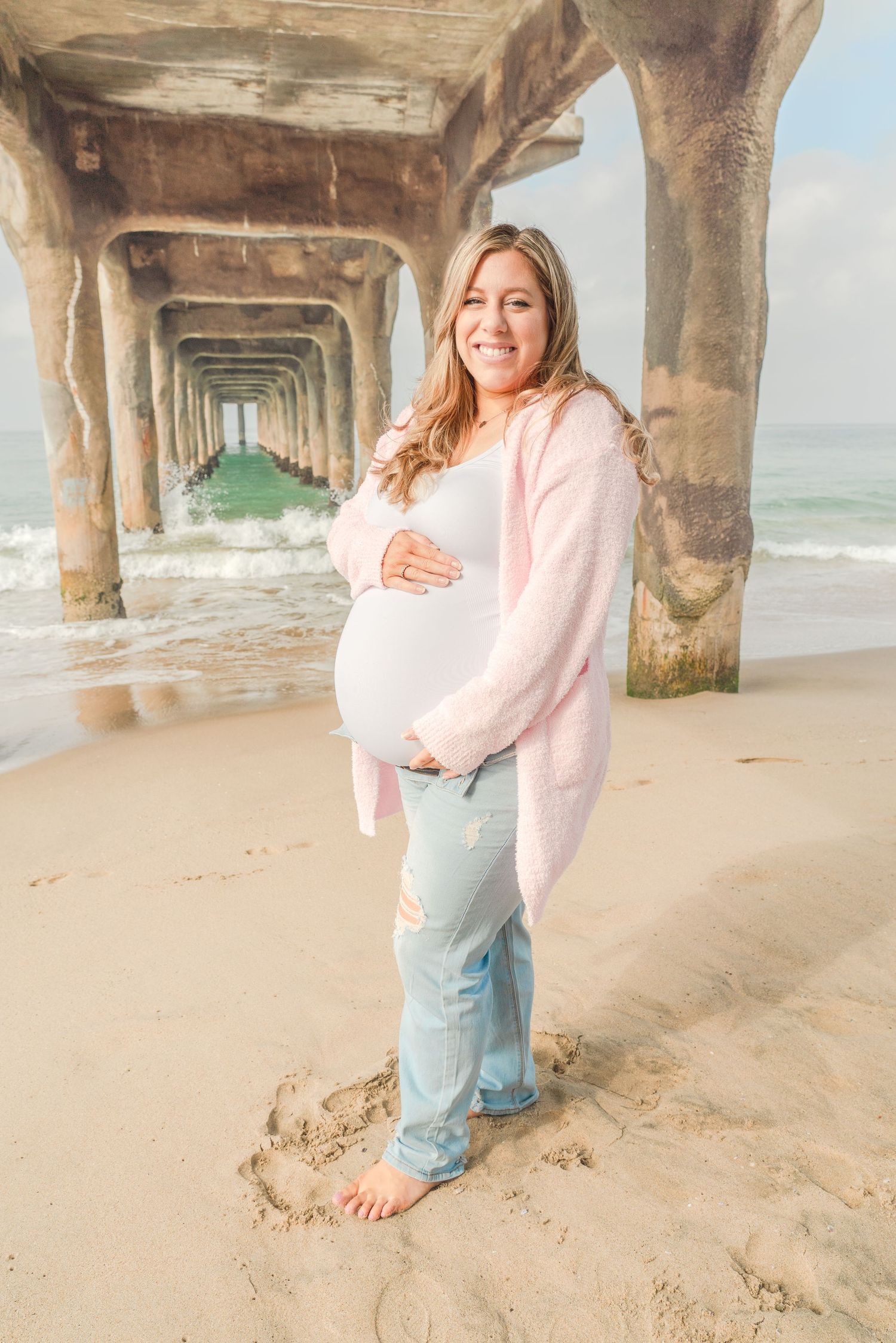 A maternity photoshoot beneath a beach pier with soft pink accents.