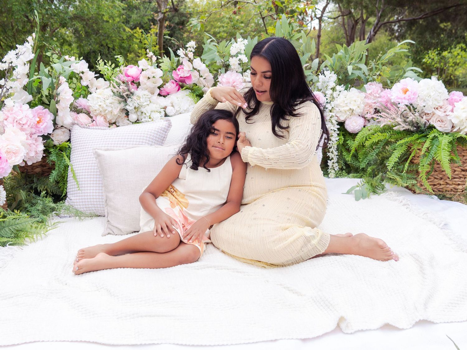 Reclining figure in cream dress poses on white blanket surrounded by pink flowers outdoors.