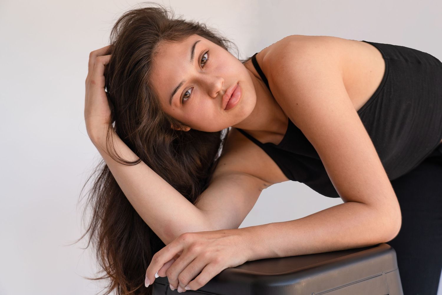 A woman in a black sleeveless top poses elegantly against a light colored background.
