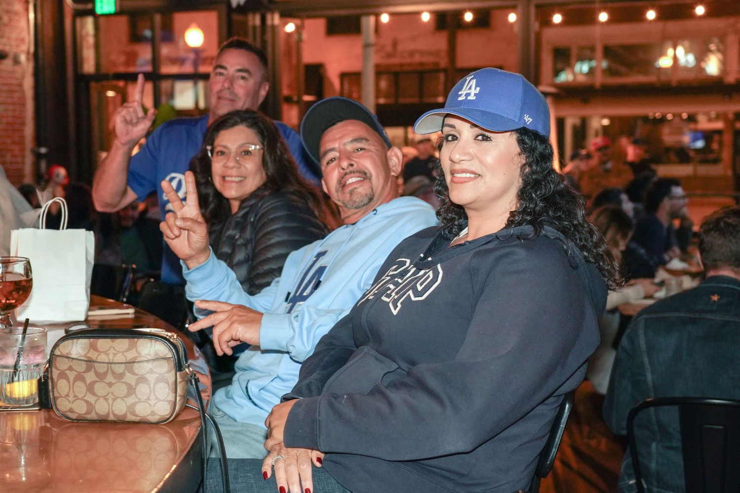 Group of friends smiling and cheering at a bar, wearing LA Dodgers gear while watching a game.