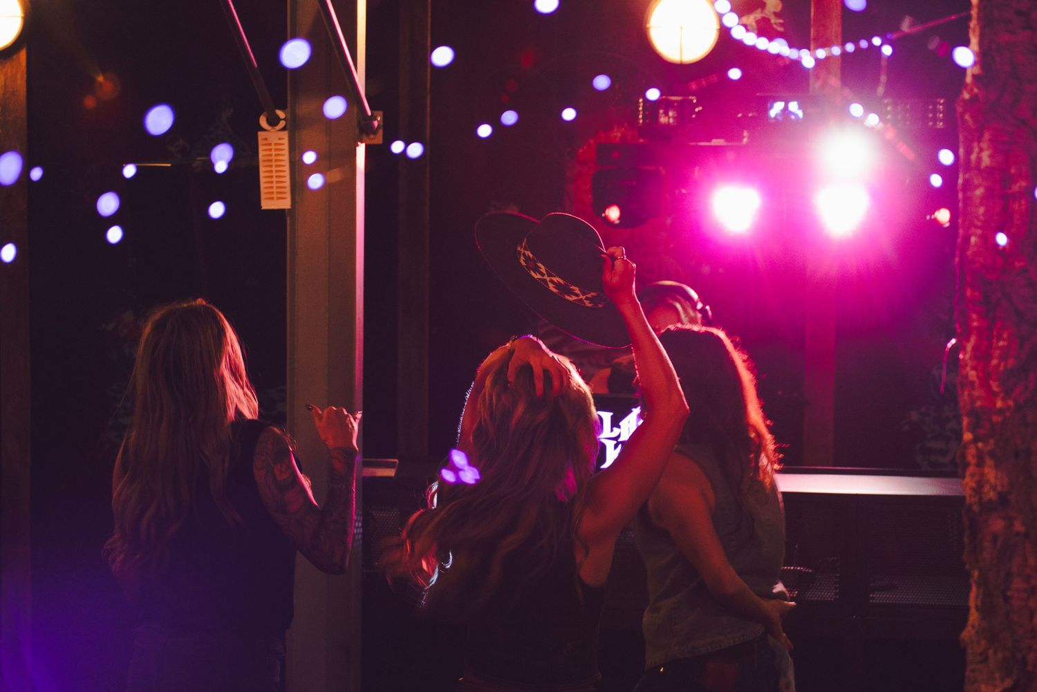 Women dancing at a vibrant nightclub with colorful bokeh lights and pink stage lighting in the background.
