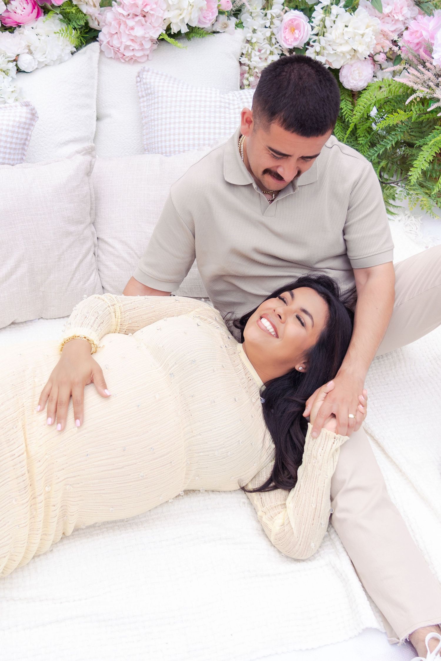 A couple shares an intimate moment on a white blanket with pink flowers in the background.