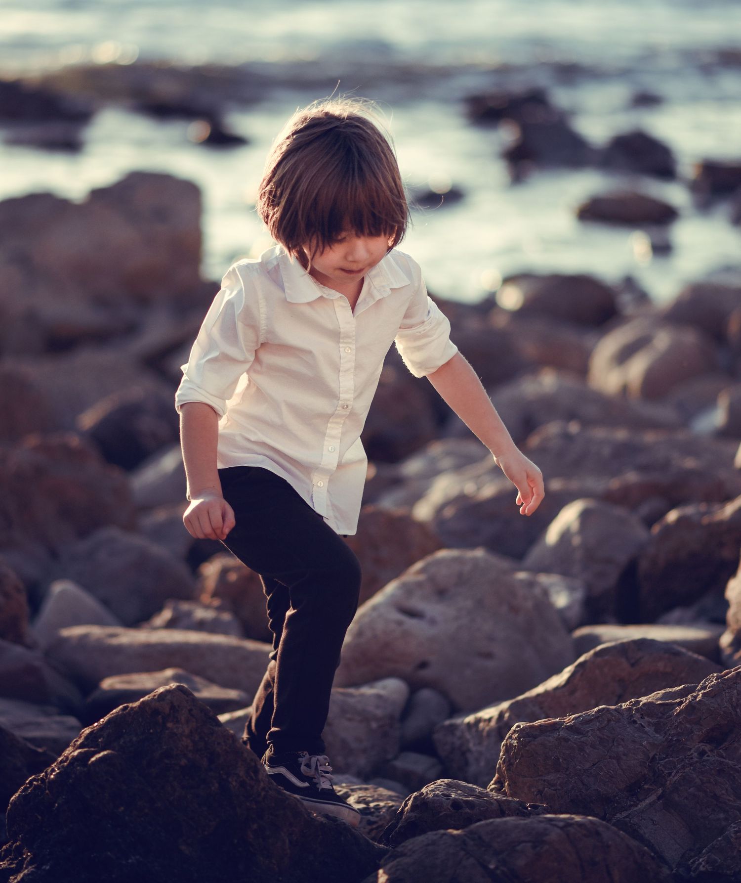 A child in a white shirt explores rocky terrain along a misty beach coastline.