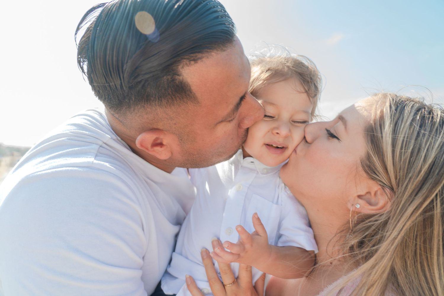 Loving family embrace captured during a beach photoshoot with bright blue sky.