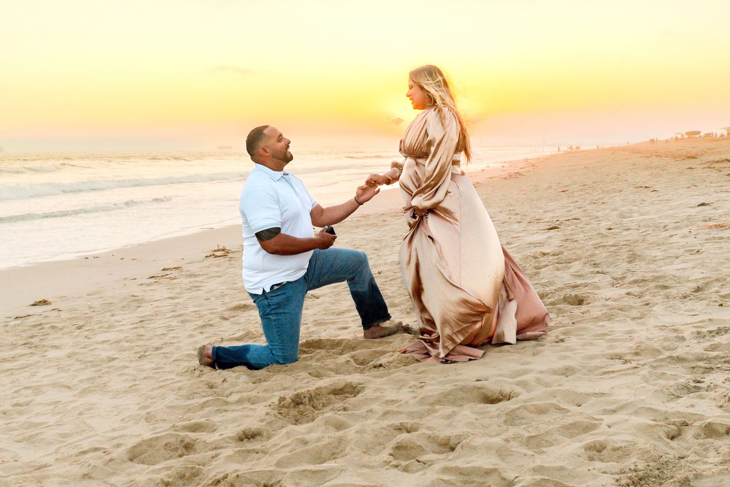 Romantic beach proposal at sunset with couple in formal attire.