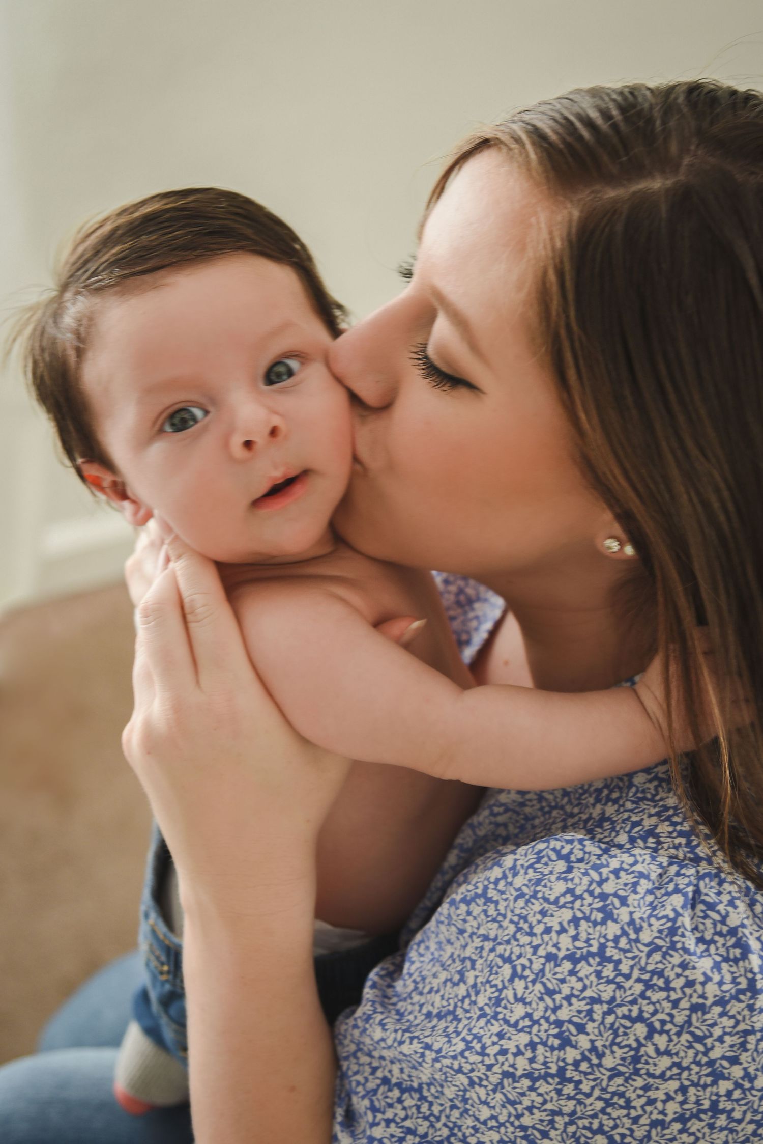 Sweet family moment with baby in floral dress against neutral backdrop.