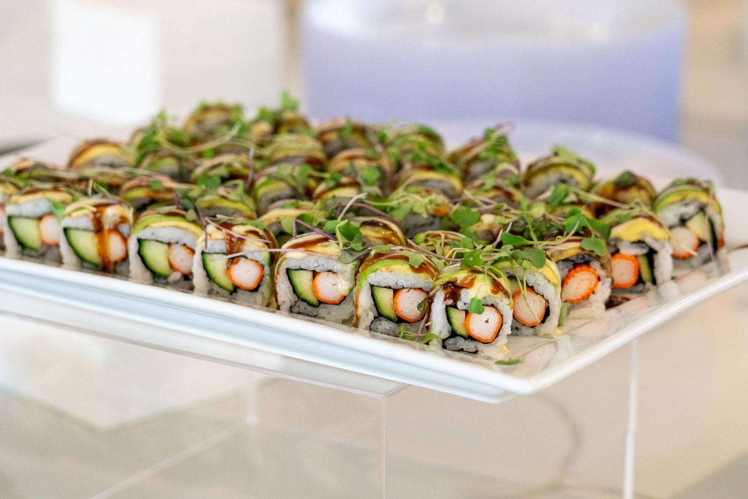 Fresh sushi rolls garnished with microgreens displayed on white serving platters.