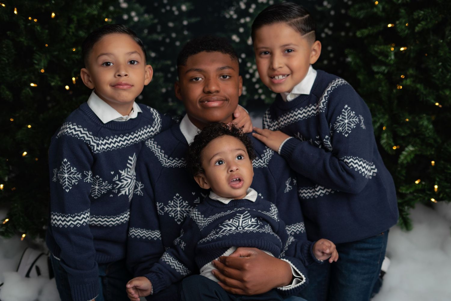 Four children wearing matching navy and white patterned sweaters pose together in front of a Christmas tree.