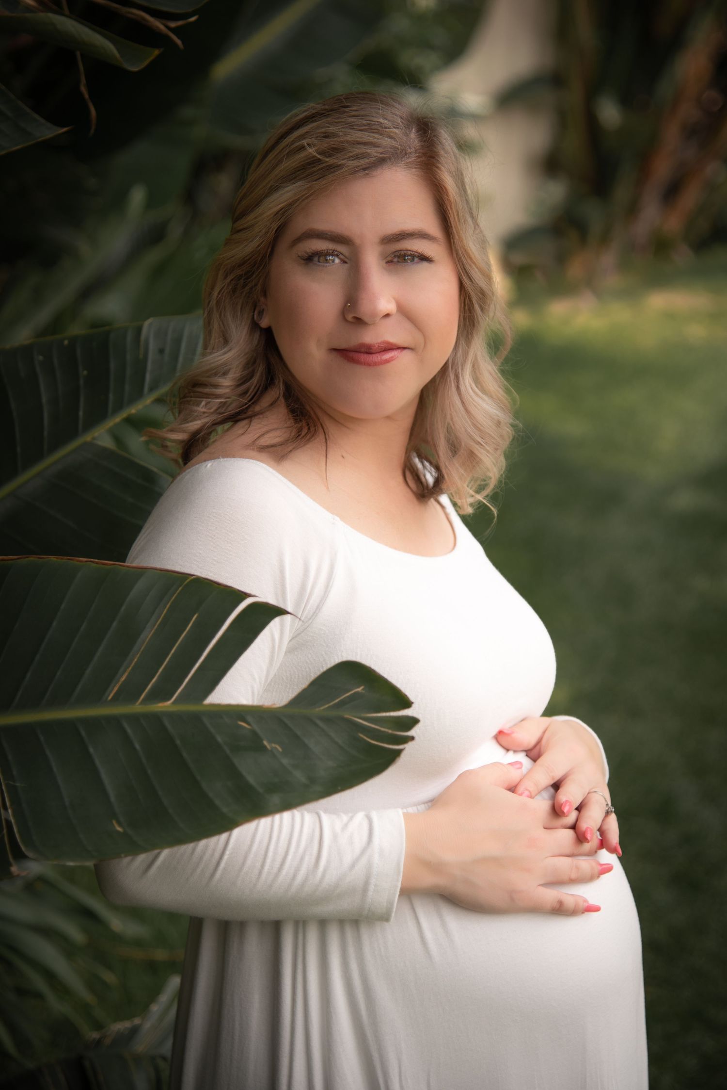 A maternity photoshoot with a woman in a white dress surrounded by tropical greenery.