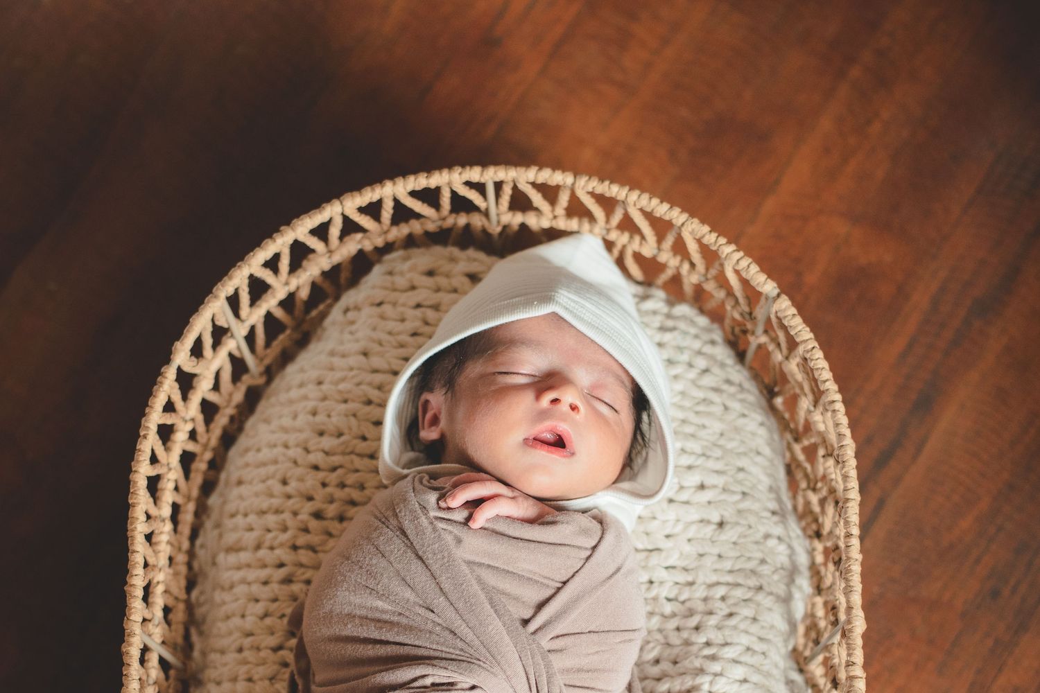 Newborn sleeping peacefully in woven basket on wooden floor.