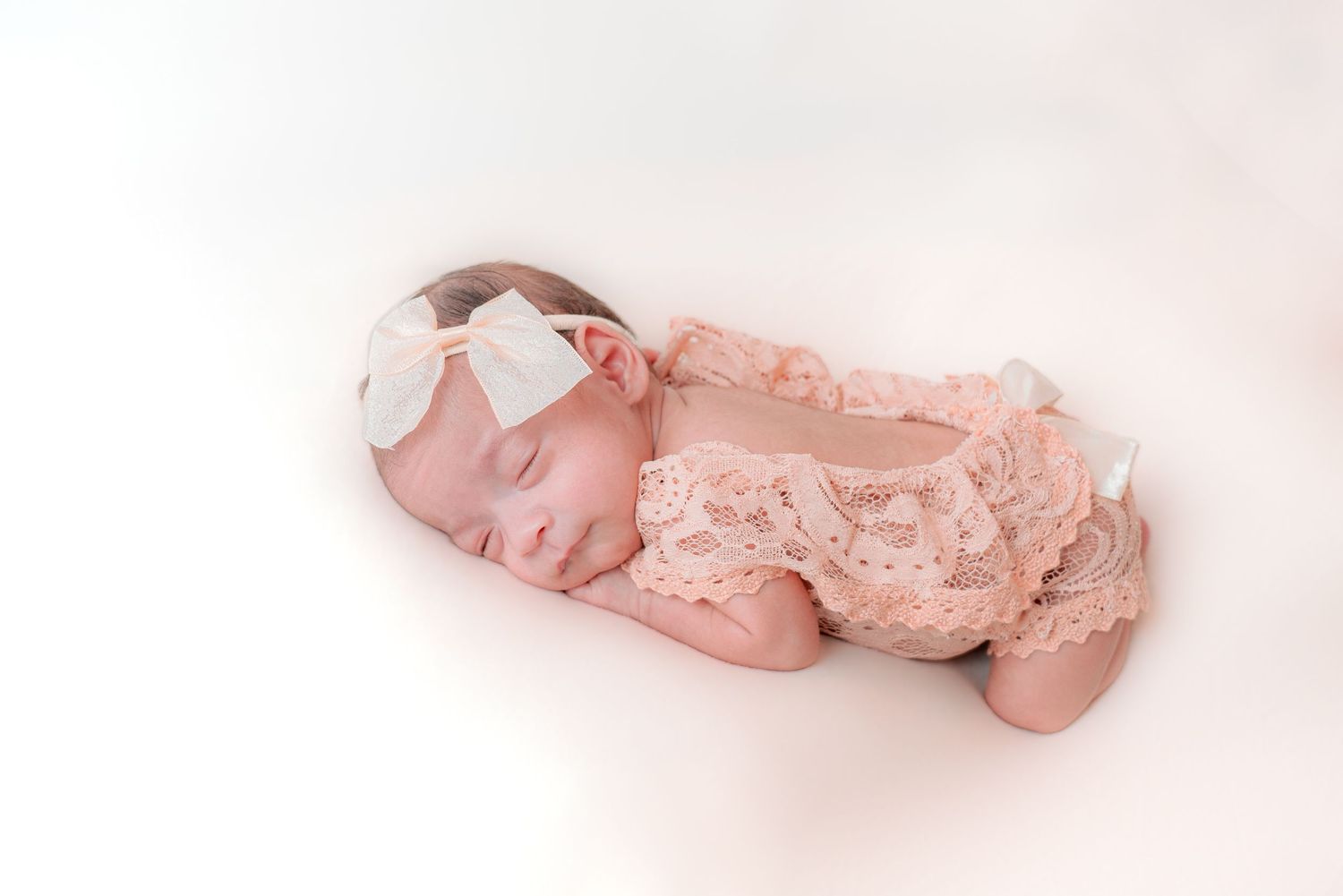 Newborn baby wrapped in delicate pink lace against light background.