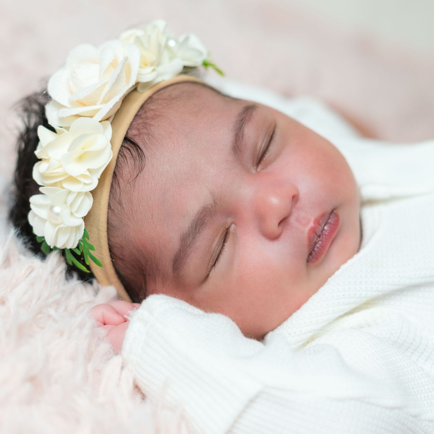 Sleeping baby wearing delicate cream floral headband against white backdrop.