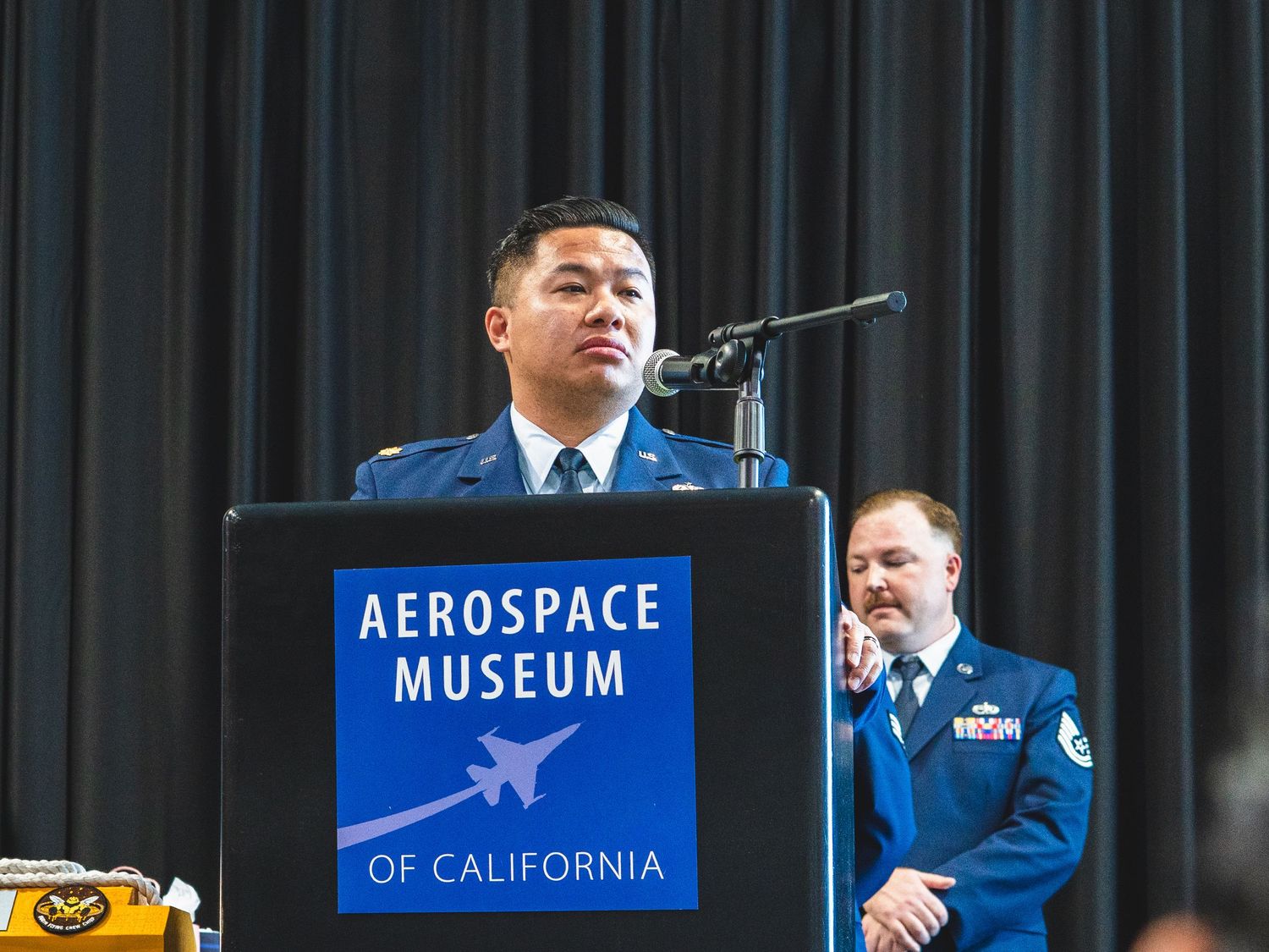 Military officer speaks at Aerospace Museum of California podium during official ceremony.