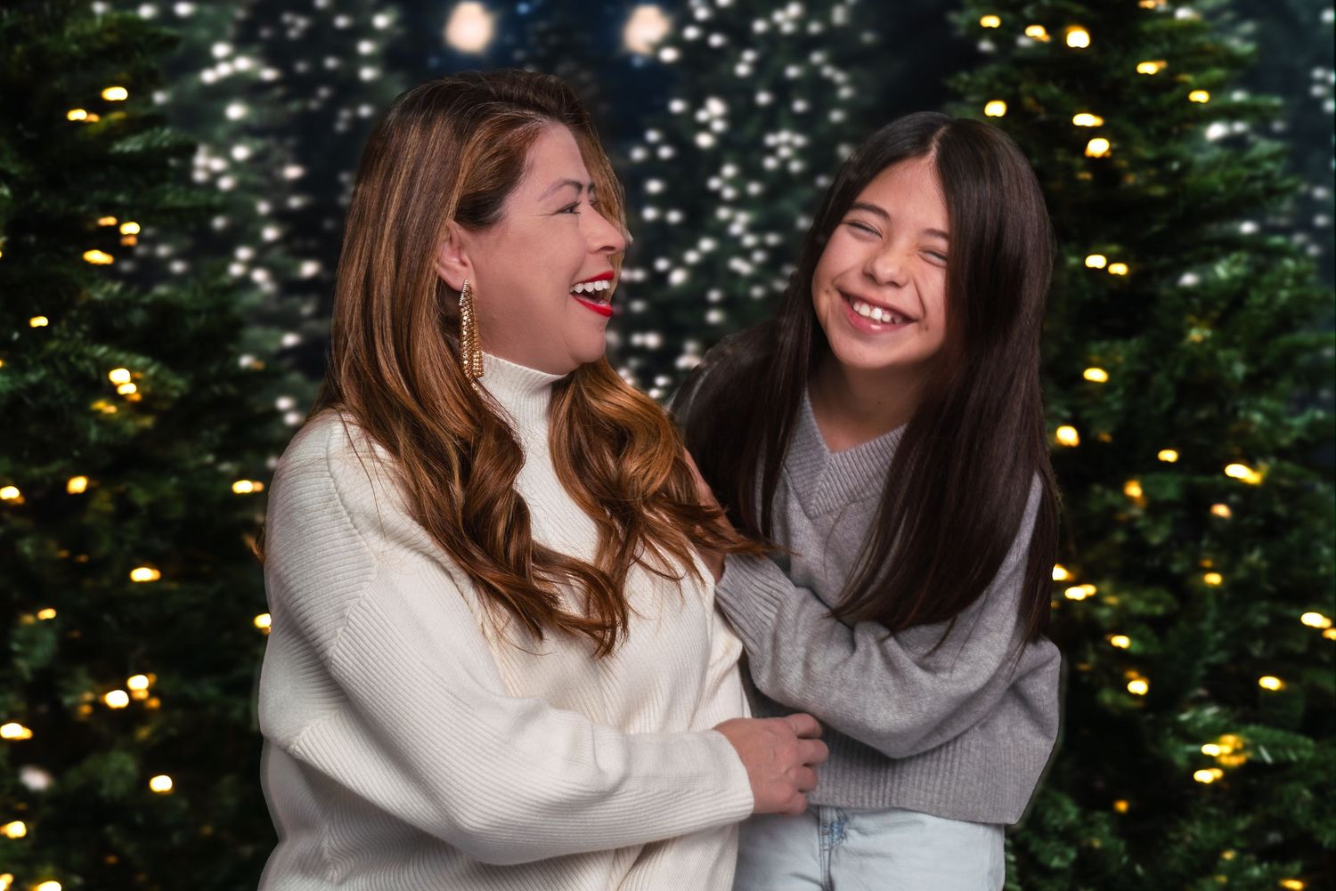 Two people laughing together while sitting outdoors with twinkling lights in the background at night.