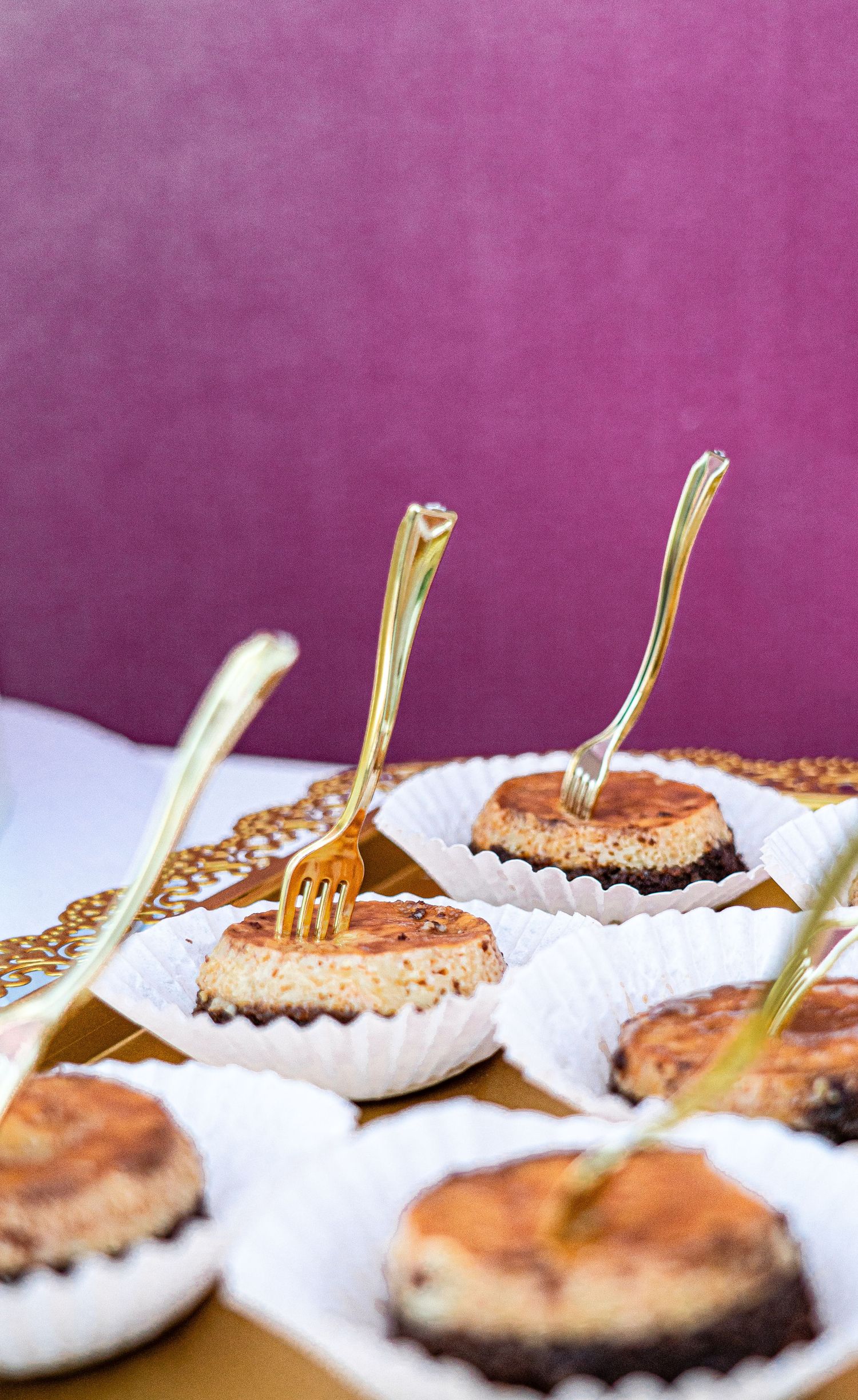 Row of elegant desserts garnished with gold utensils on white serving plates.
