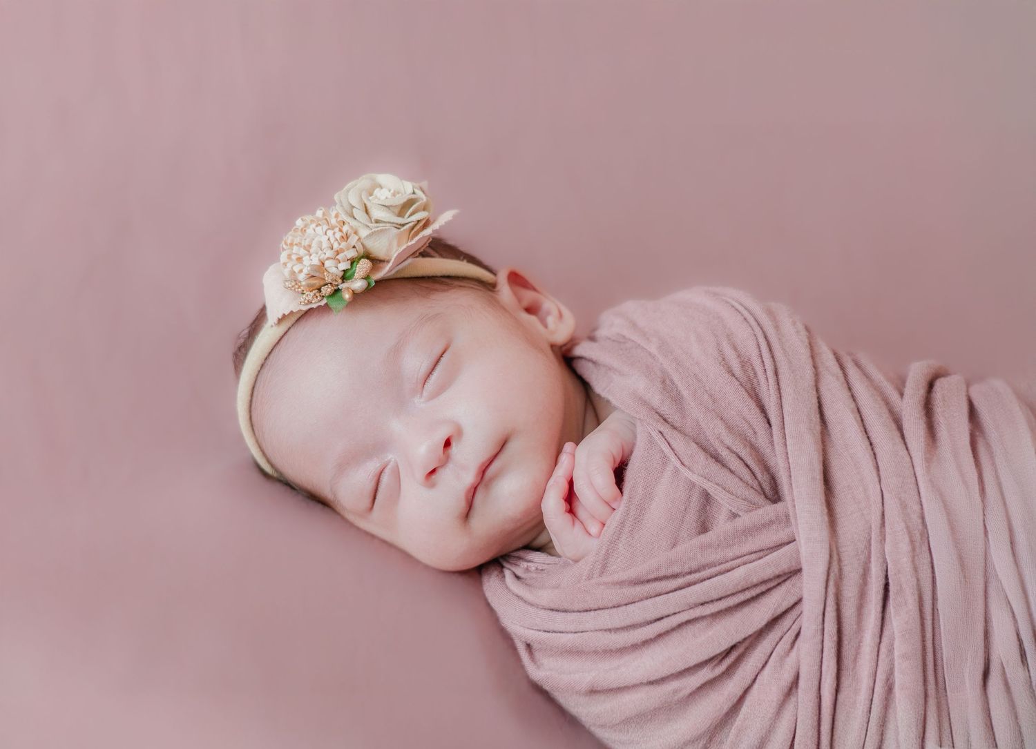 Close-up view of a baby sleeping peacefully wrapped in soft pink fabric.