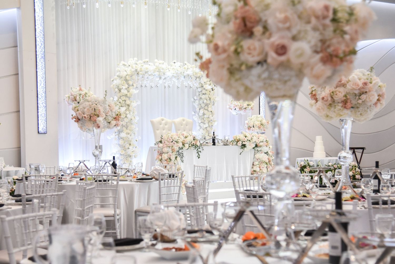 White and blush wedding reception decor featuring elegant table settings and dramatic floral arrangements.